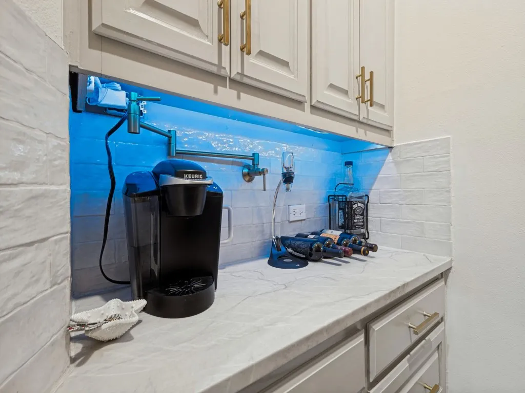 Built-in custom cabinetry with gold-tone hardware, under-cabinet lighting, a white subway tile backsplash, and a light-toned countertop