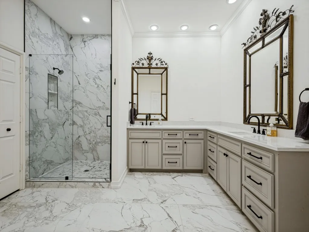 Spacious bathroom featuring a glass-enclosed shower with a tiled interior, dual vanity with light-toned cabinetry, white countertops, and expansive floor tiling