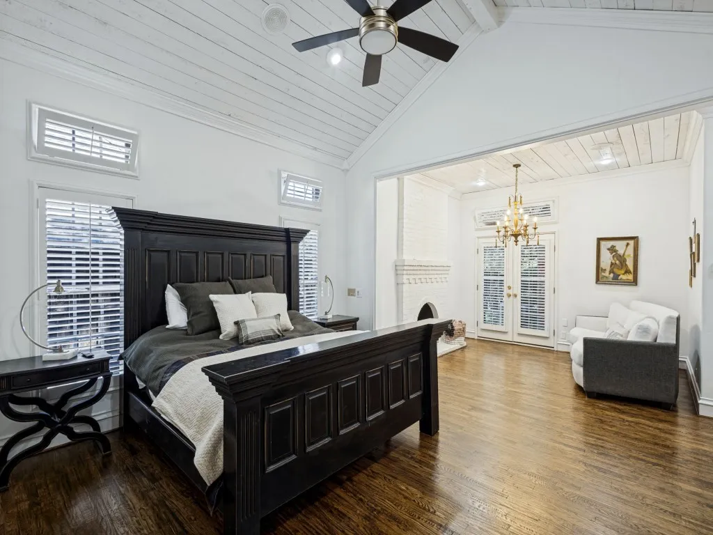Vaulted ceiling with wood-finish planks, wood-finish flooring, plantation shutters, French doors, and a decorative fireplace