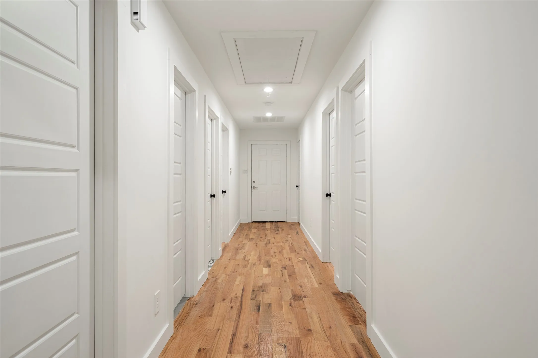 Hallway featuring wood-finish flooring, recessed lighting, white walls, and modern paneled doors with black hardware