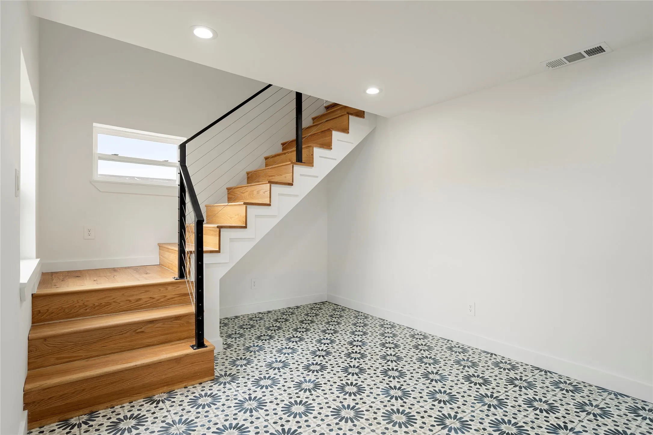 Open staircase featuring natural wood treads, a contemporary black metal and cable railing, and white risers