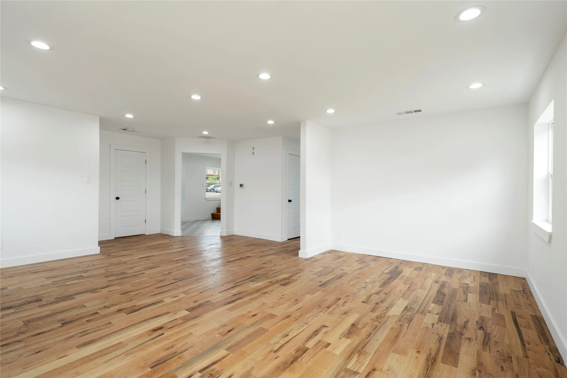 Spacious interior room featuring wood-finish flooring, white walls, recessed ceiling lighting, and white baseboards
