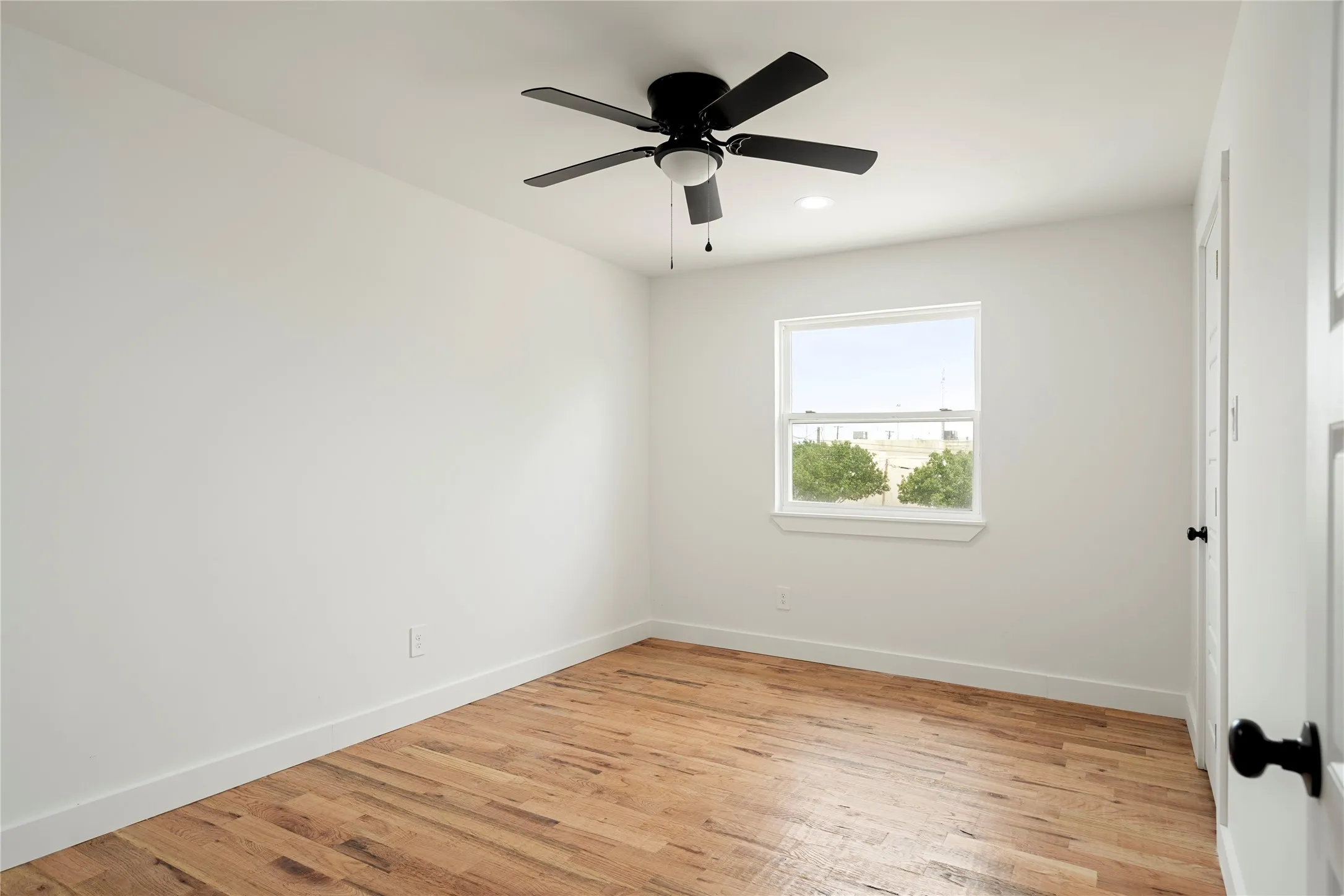 Spacious room featuring wood-finish flooring and a ceiling fan with integrated lighting