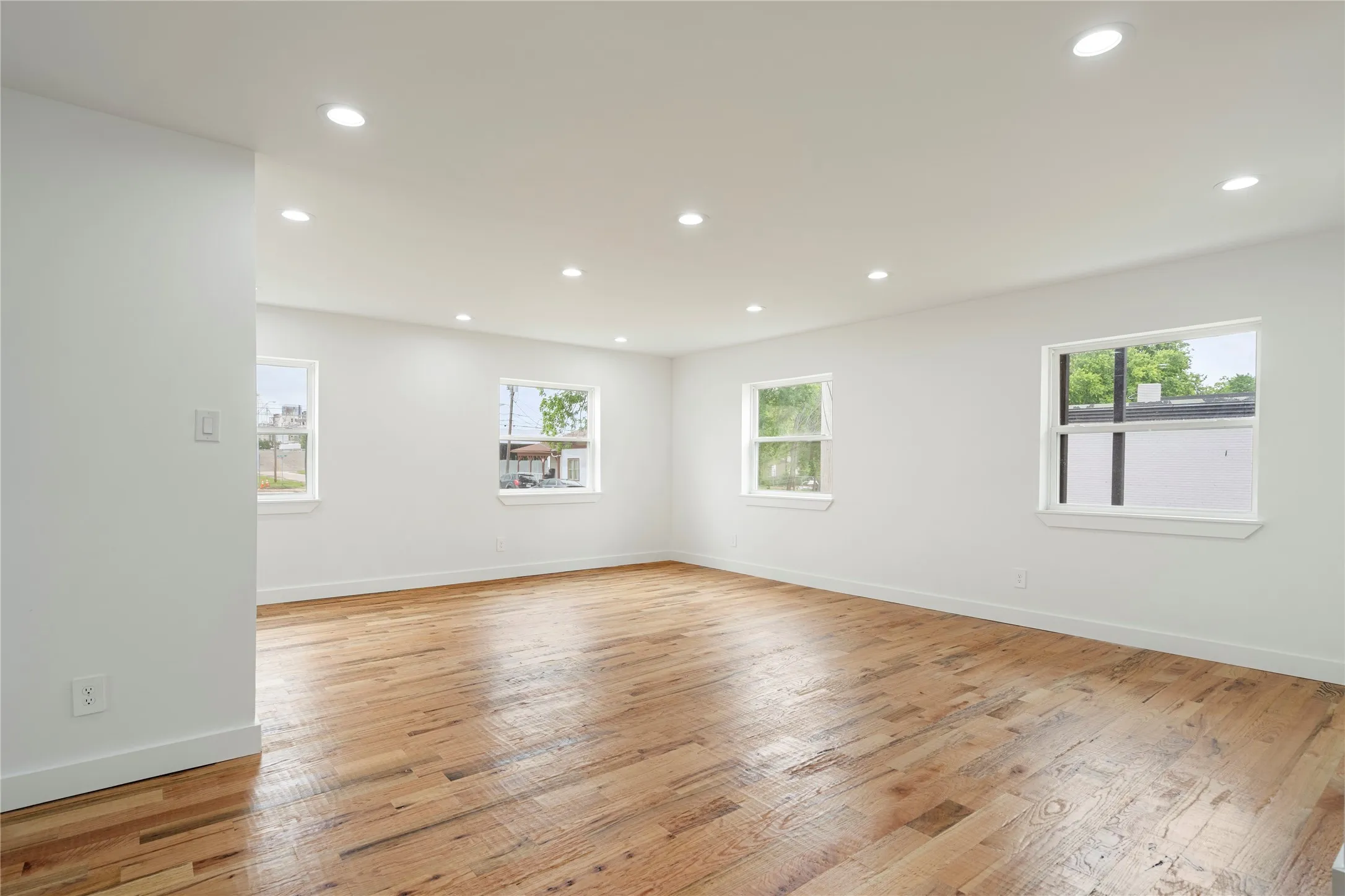 Spacious room featuring wood-finish flooring, white walls, multiple windows, recessed lighting, and white baseboards
