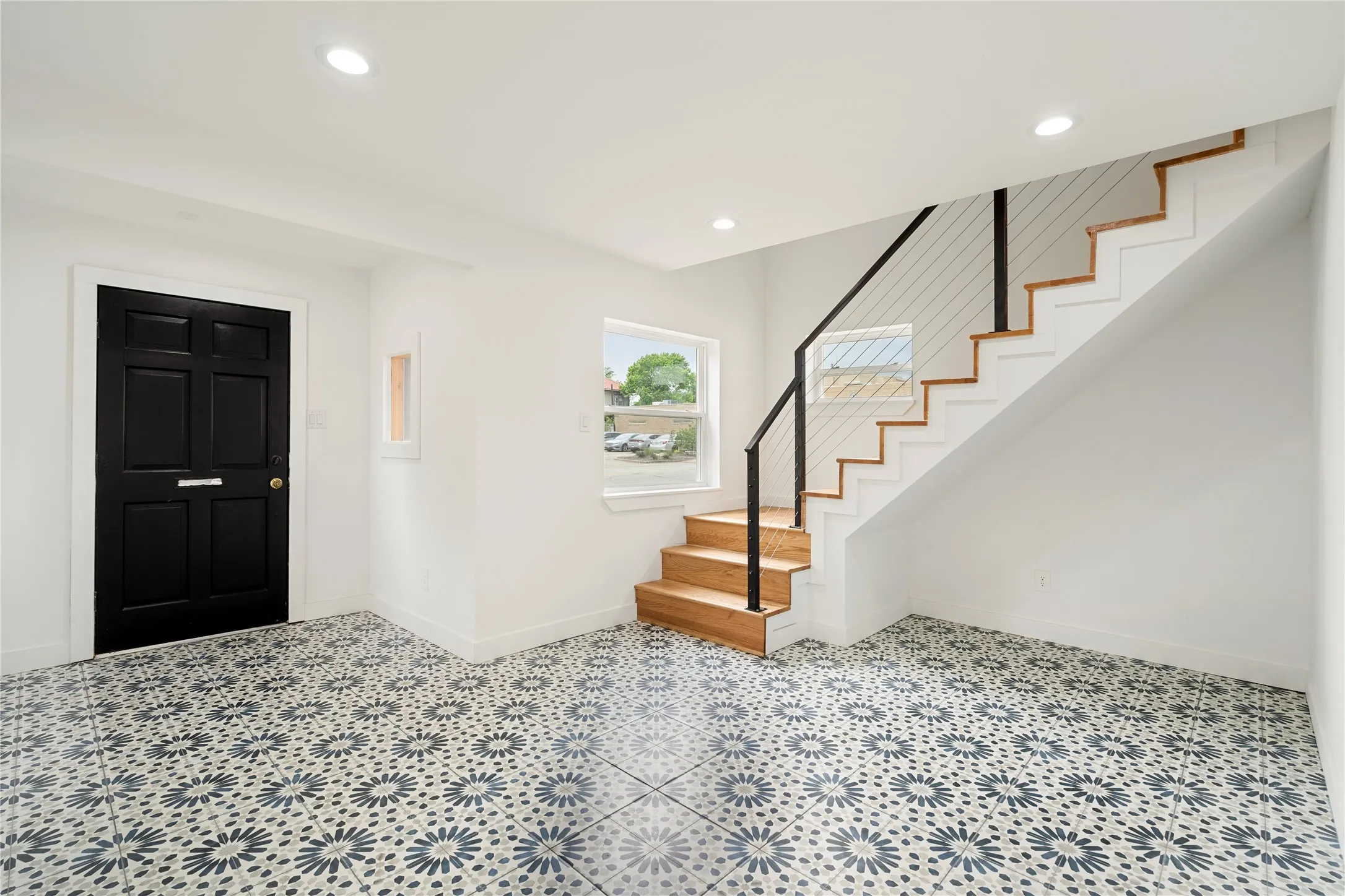 Entryway featuring patterned tile flooring, a six-panel black door, a contemporary staircase with wood treads and a cable railing system, recessed lighting, and a window