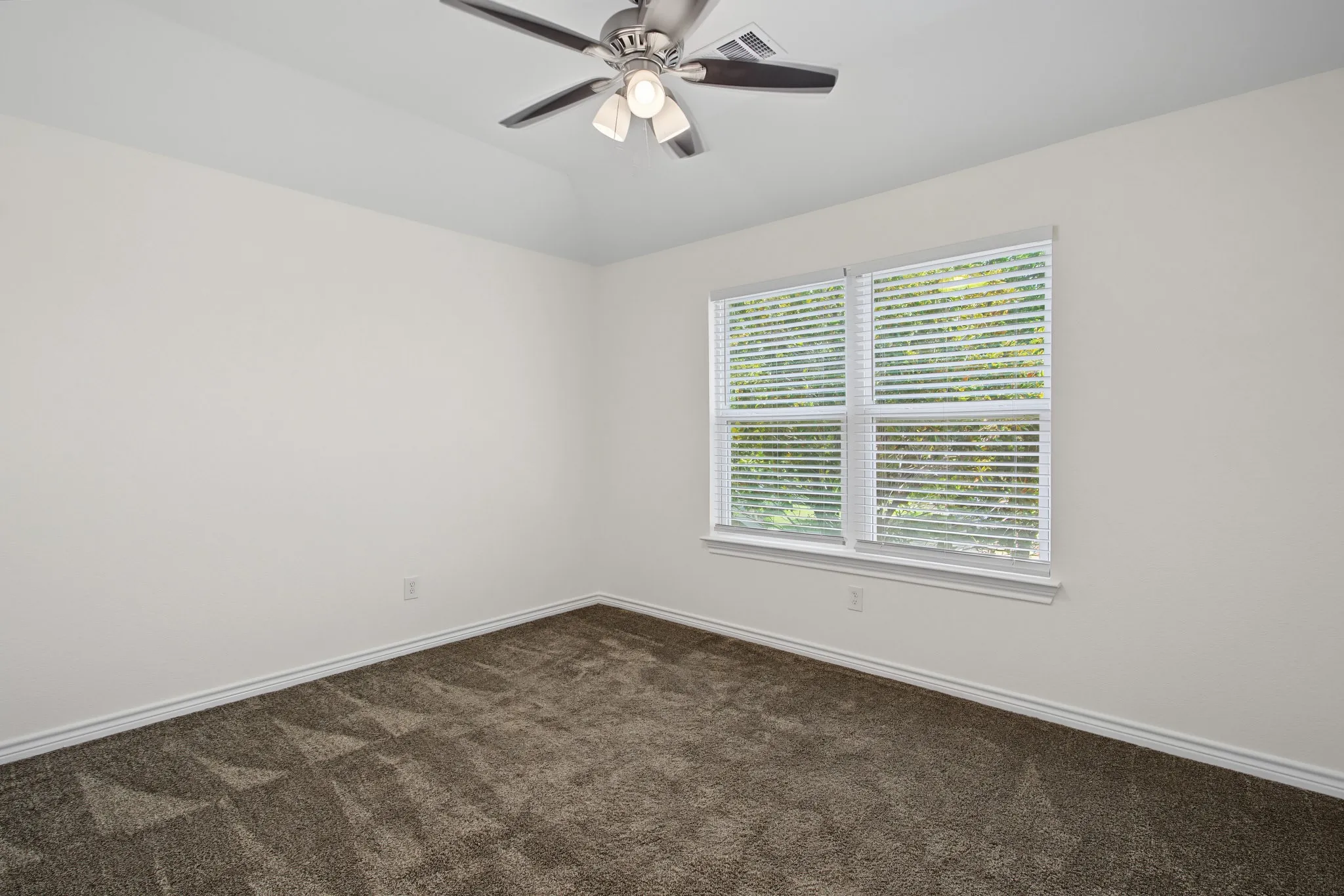 Tray ceiling with a ceiling fan light fixture, two-pane window with blinds, and neutral carpeting