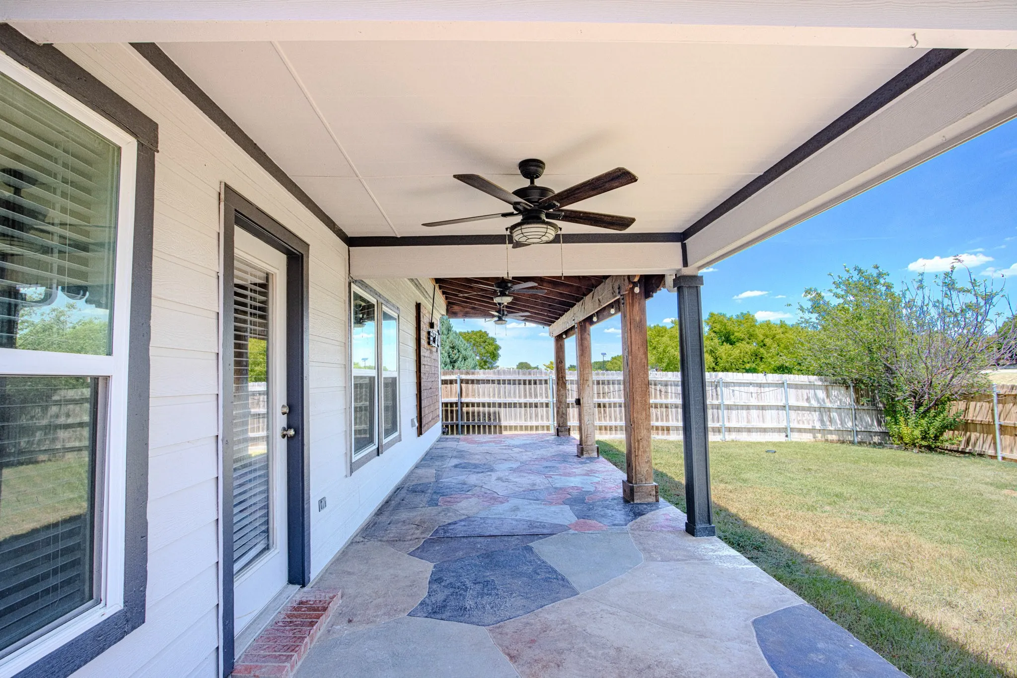Covered patio with flagstone-style flooring, dual ceiling fans, and wood support beams