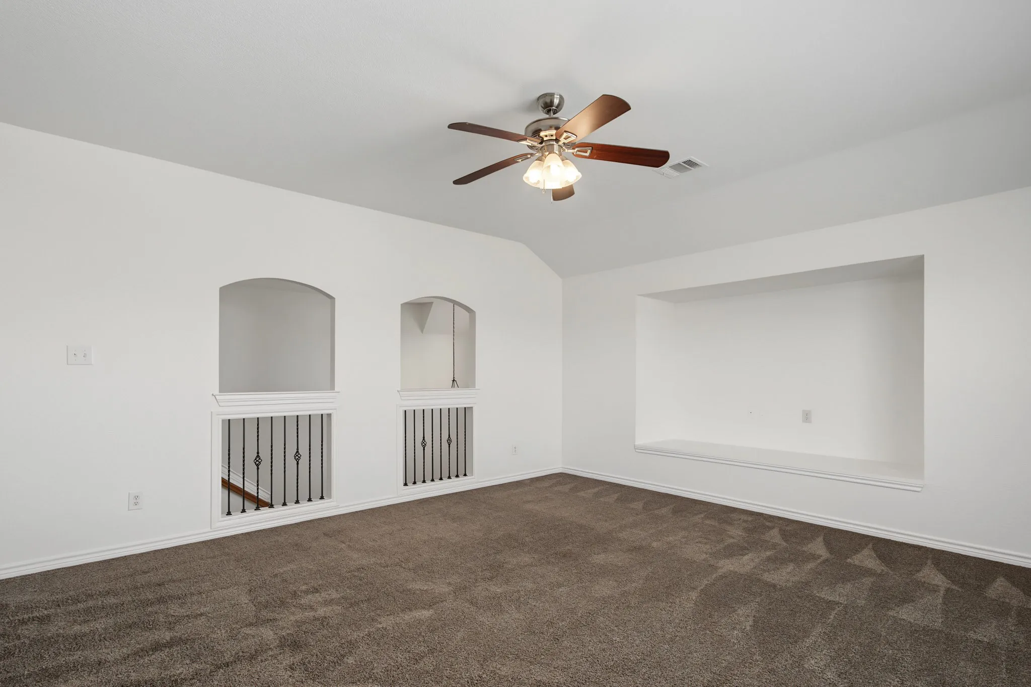 Vaulted ceiling with a ceiling fan, plush carpet flooring, recessed wall niche, and arched wall openings with decorative railings