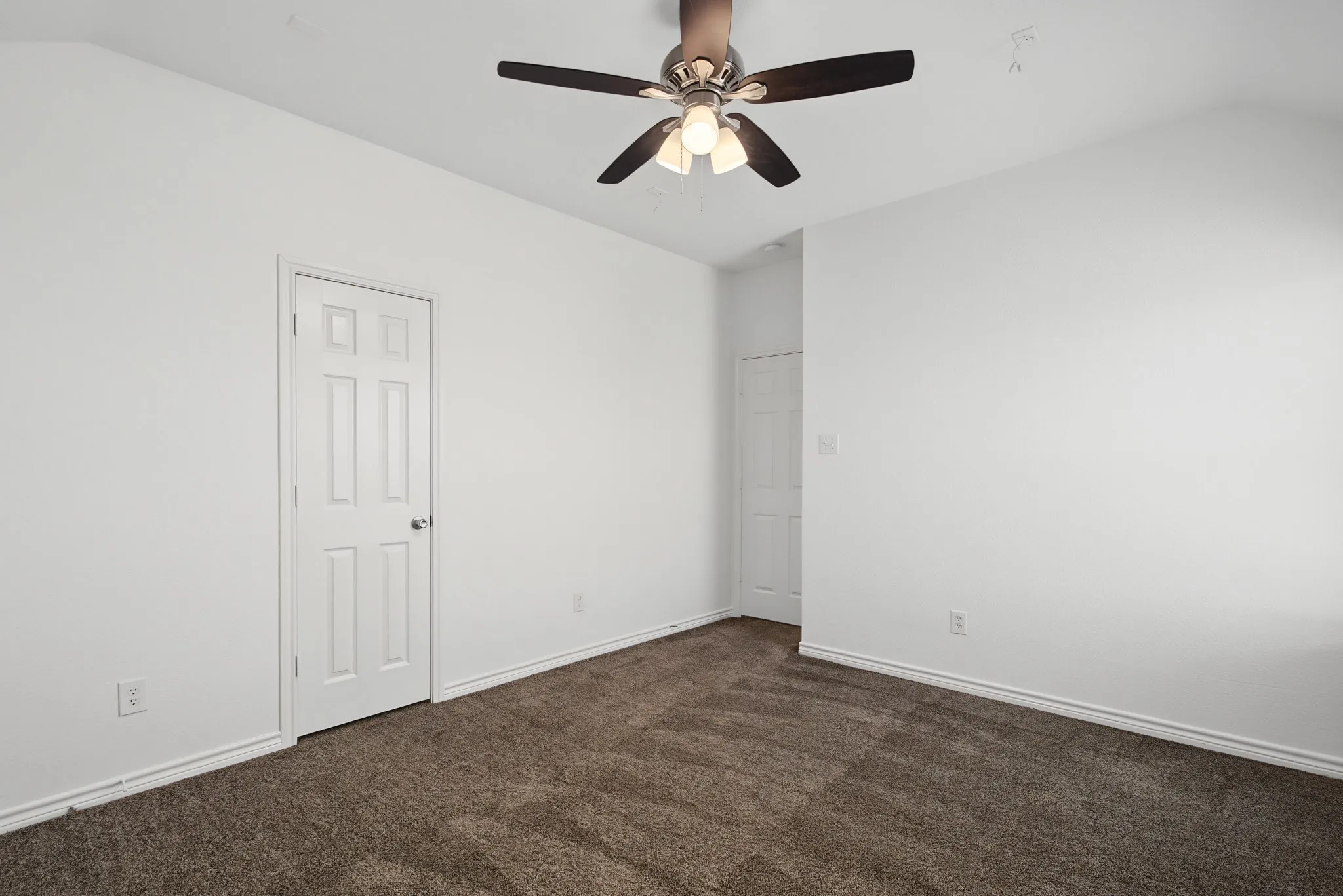Vaulted ceiling with an attached ceiling fan, two panel doors, and neutral carpeting