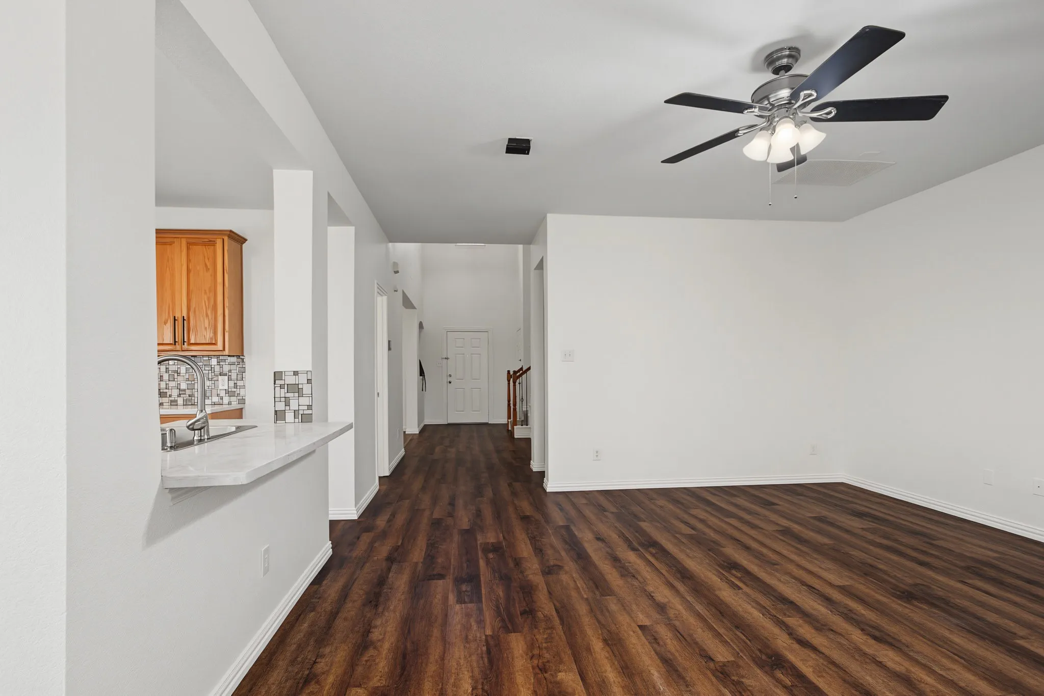 Wood-finish flooring throughout, bright white walls, and a ceiling fan with integrated lighting