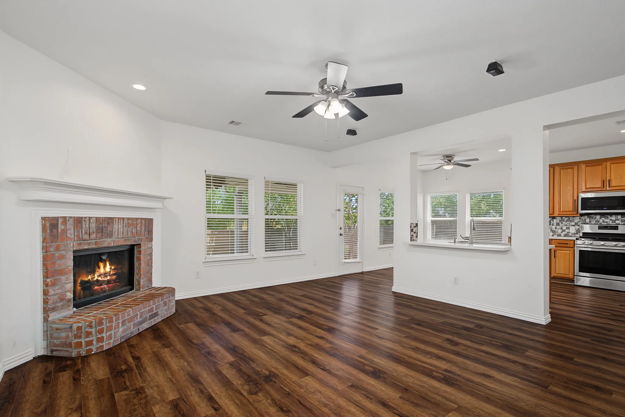 Expansive room featuring rich wood-finish flooring, a brick fireplace with a white mantel, and multiple windows