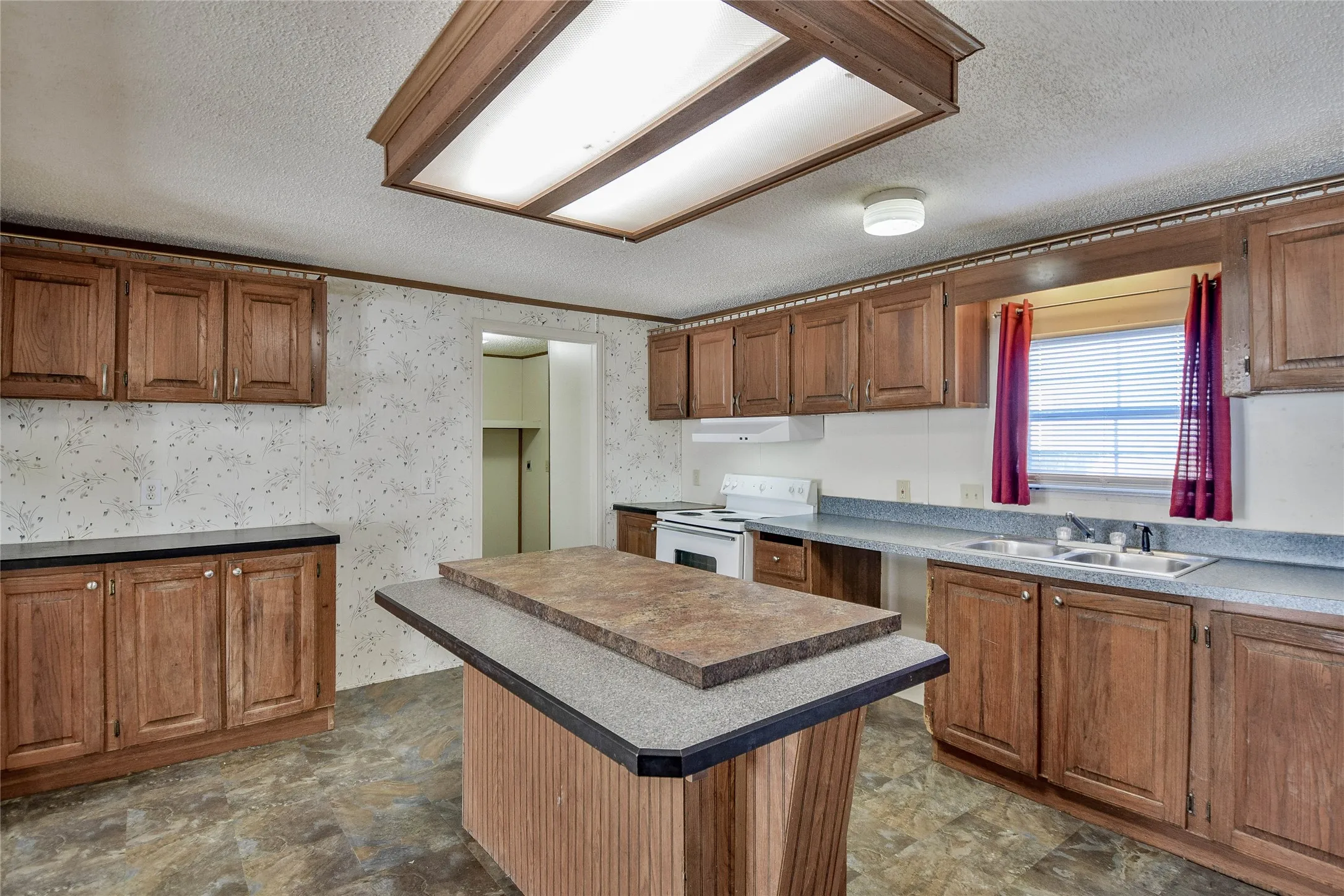 Kitchen featuring wood-finish cabinetry, a central island with a multi-level countertop, a built-in double basin sink, and an overhead fluorescent lighting fixture