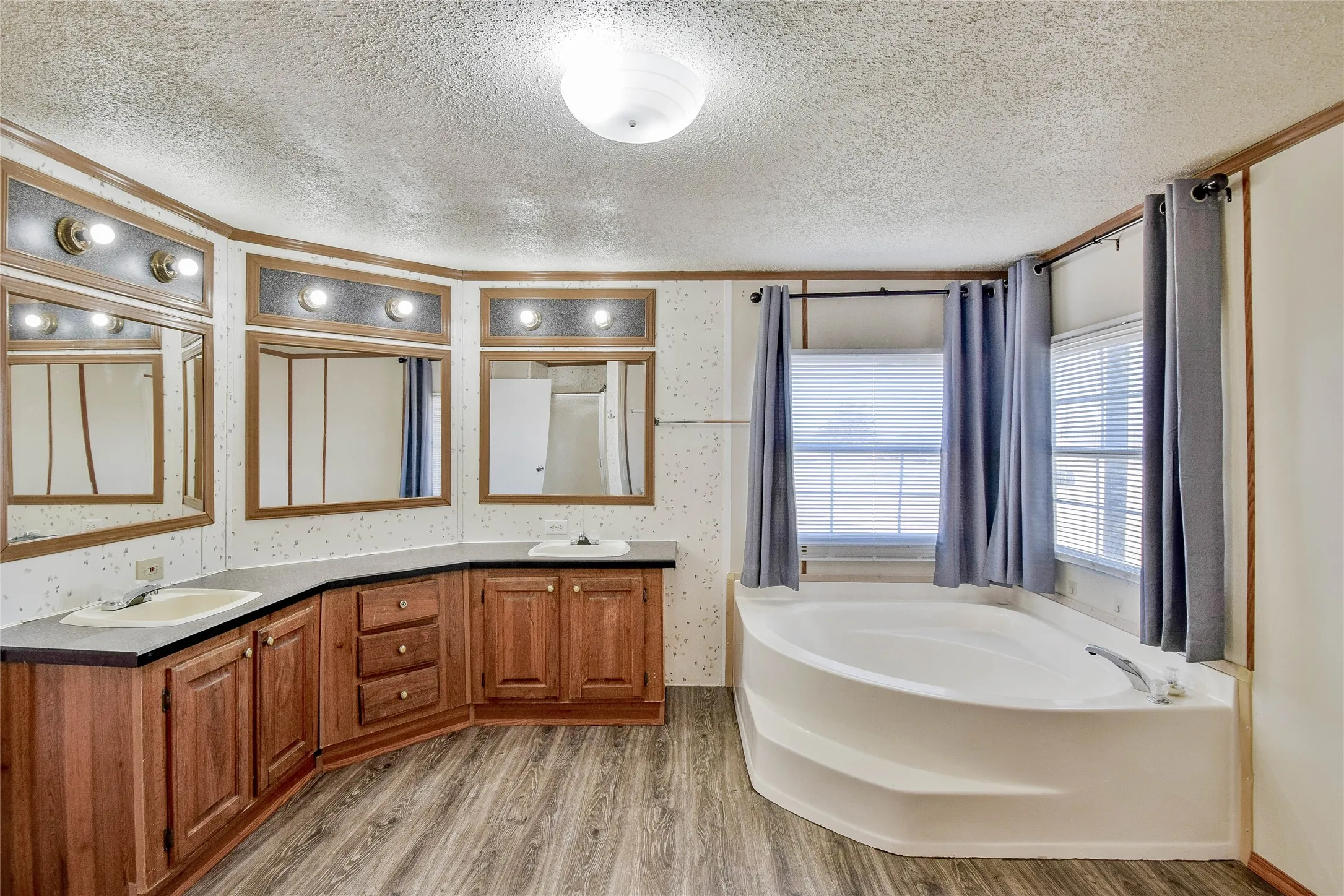 Dual vanities with integrated sinks, ample wood cabinetry, wood-finish flooring, built-in soaking tub, and multiple windows