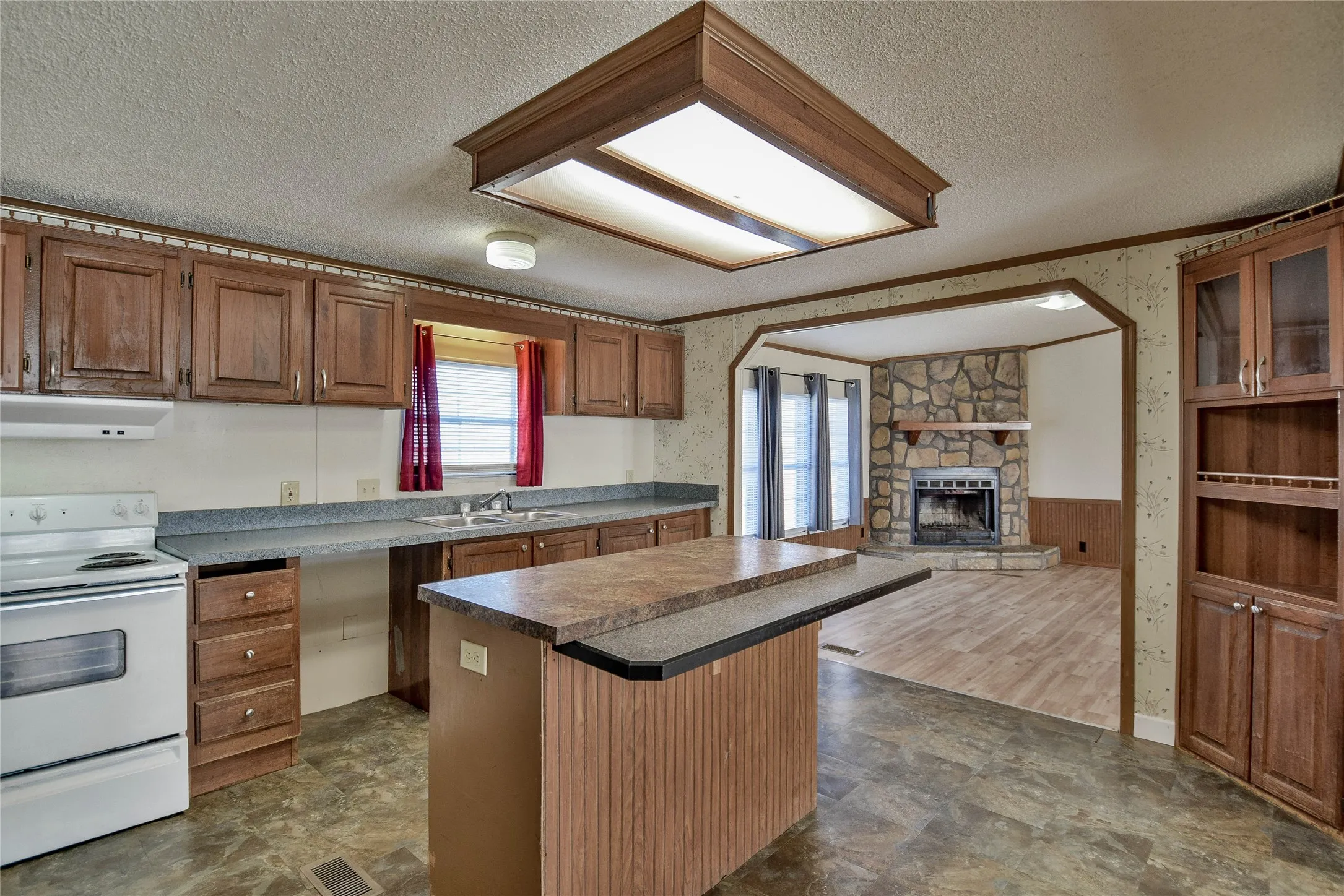 Kitchen featuring wood cabinetry, a center island, and a stone-faced fireplace visible in the adjacent room