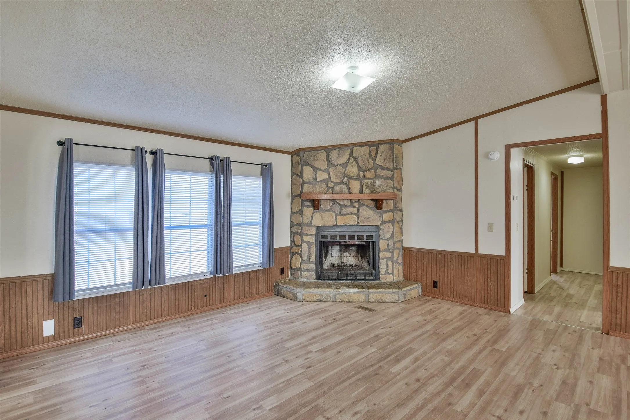 Corner stone fireplace with a wood-finish mantel, wood-finish flooring, and multiple windows