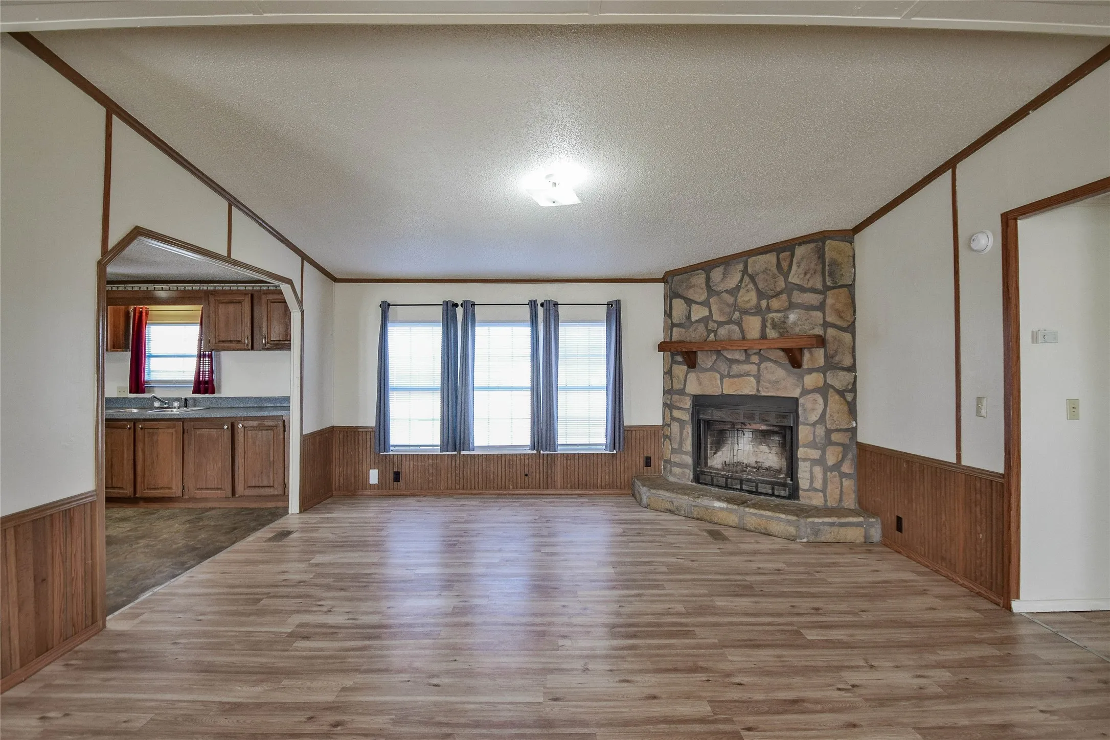 Stone-clad fireplace with wood mantle, wood-finish flooring, and built-in wood cabinetry in the kitchen