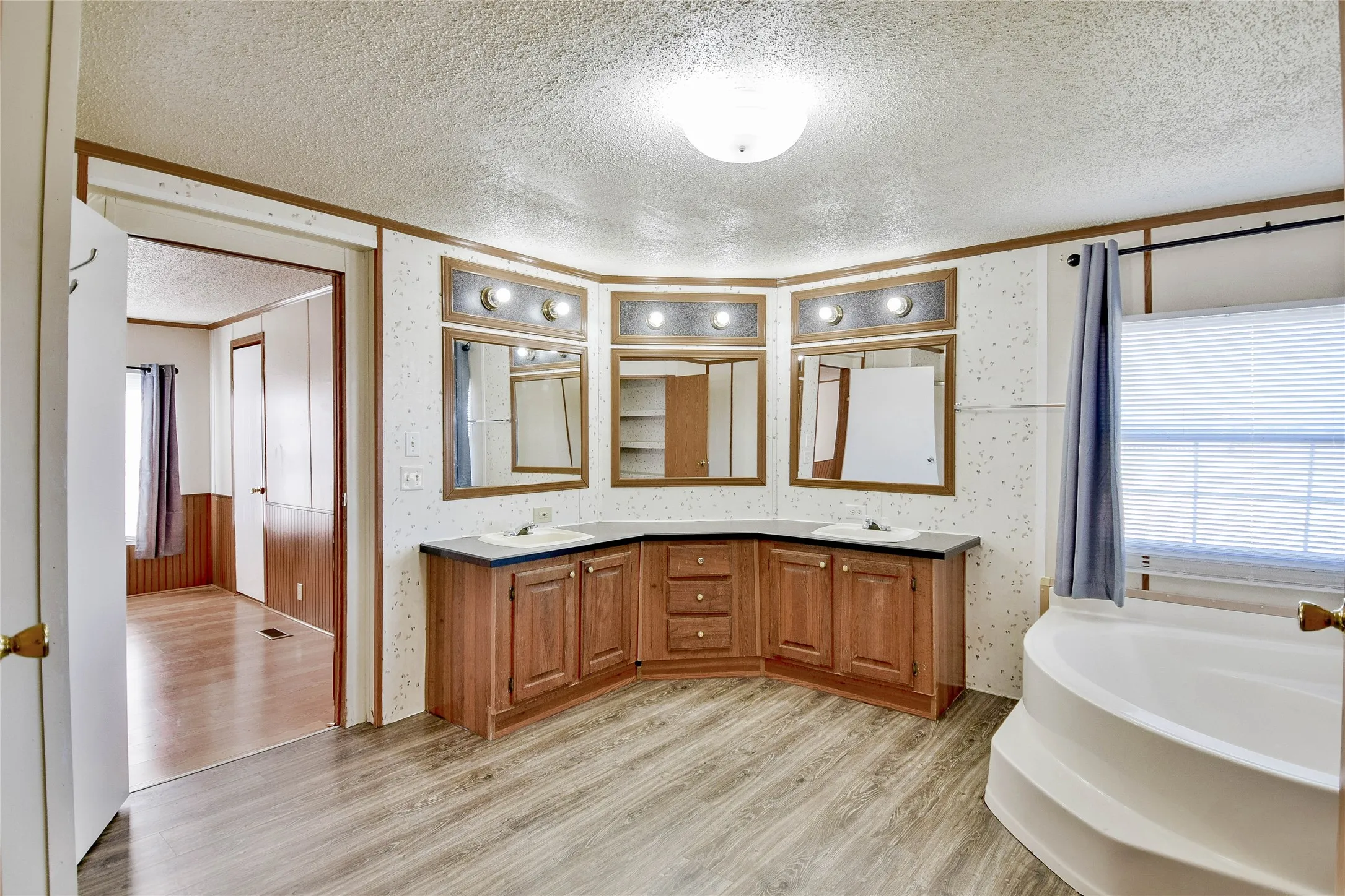 Dual sink vanity with wood-finish cabinetry, a built-in corner bathtub, and wood-finish flooring