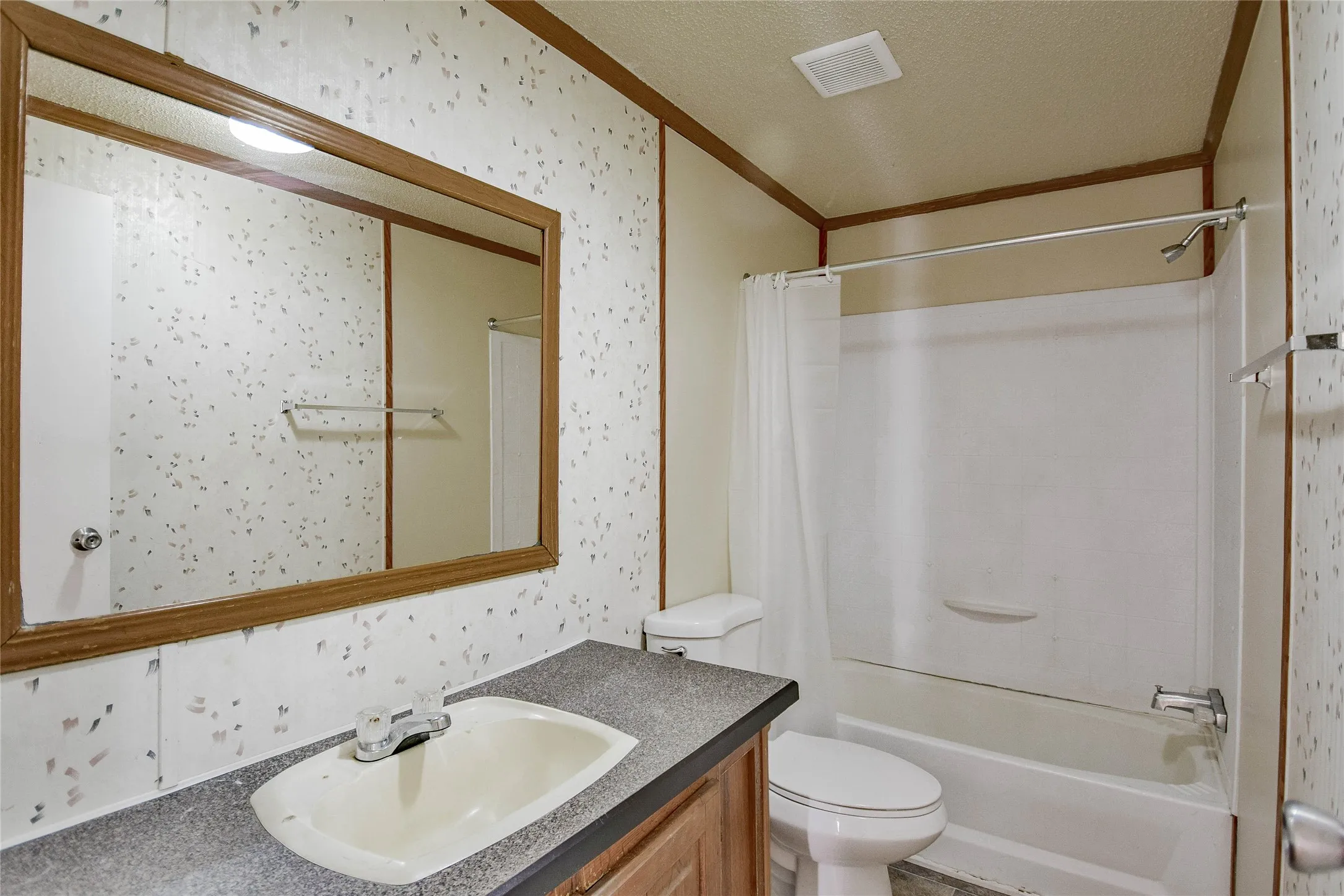 Bathroom featuring a vanity with an integrated sink, a large wall-mounted mirror, and a built-in shower/tub combination with a shower curtain rod