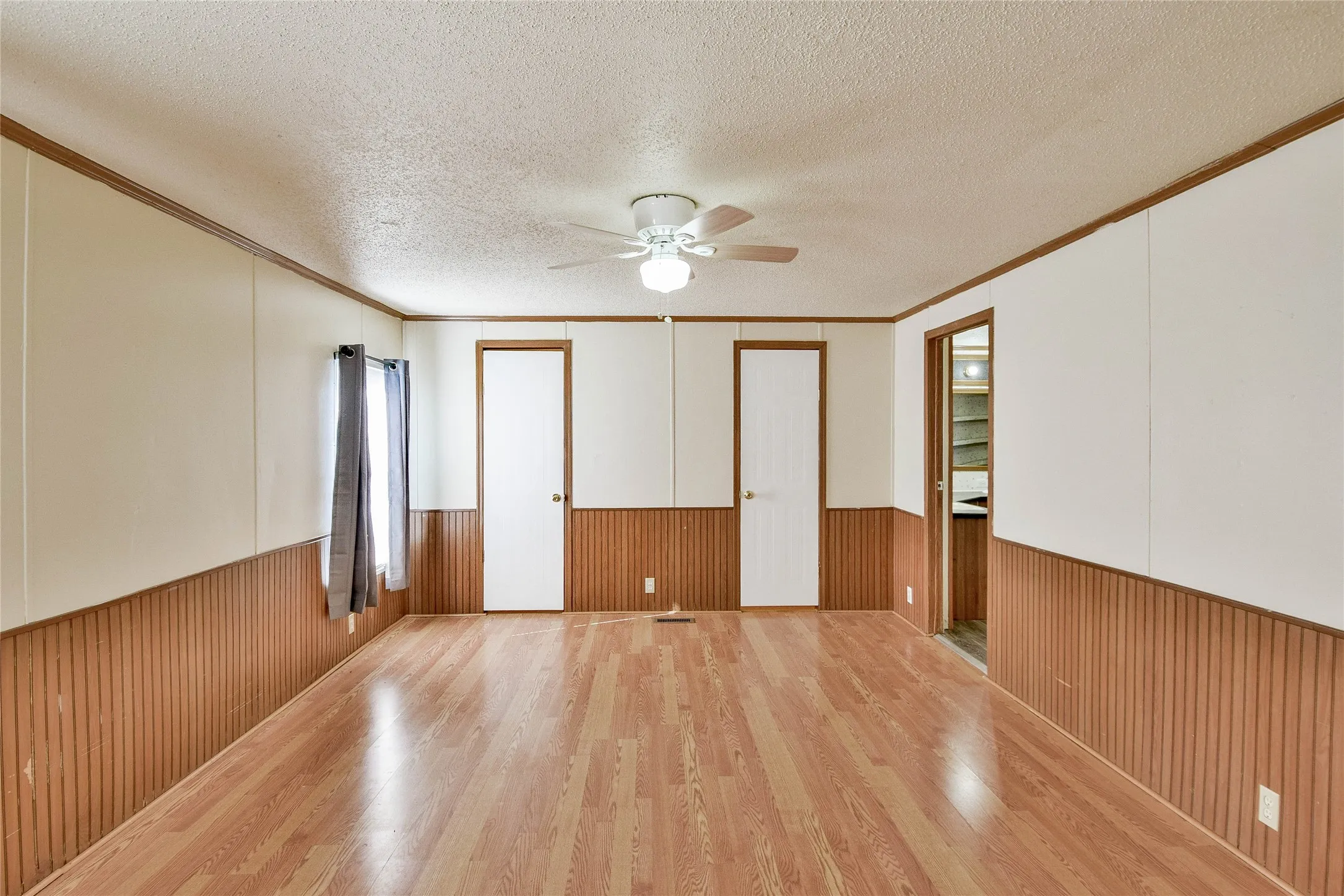 Wood-look vinyl  flooring, two-tone wall paneling with vertical wood texture, and a ceiling fan with integrated lighting