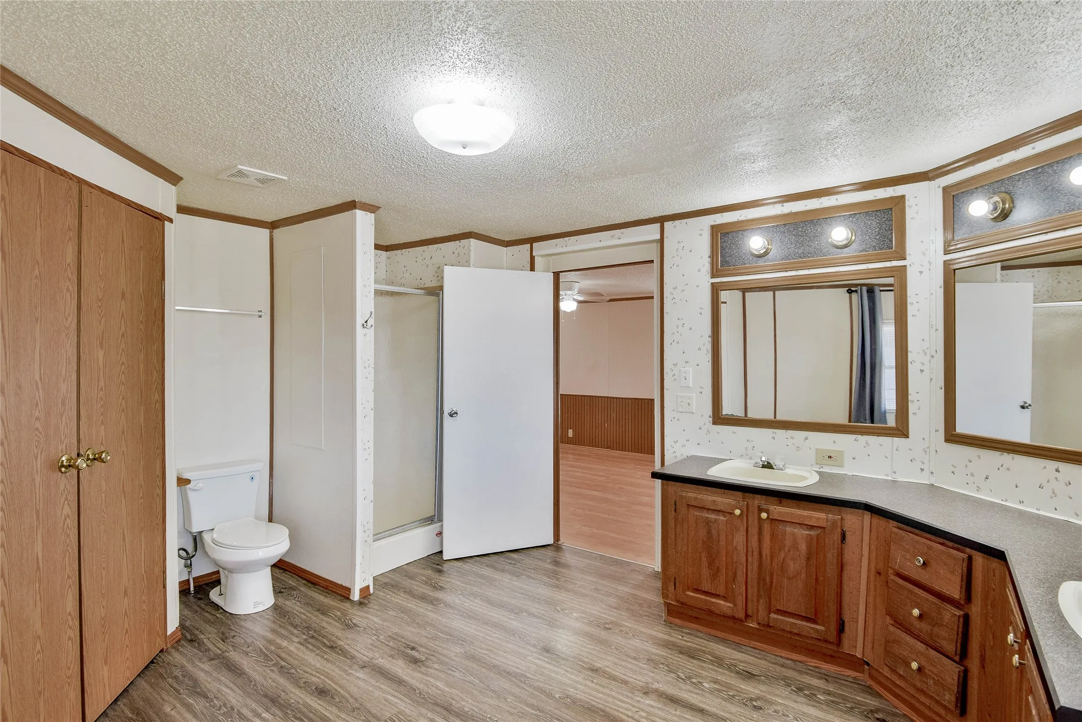 Dual sink vanity with wood-finish cabinetry, a walk-in shower, wood-finish flooring, and a flush-mount ceiling light