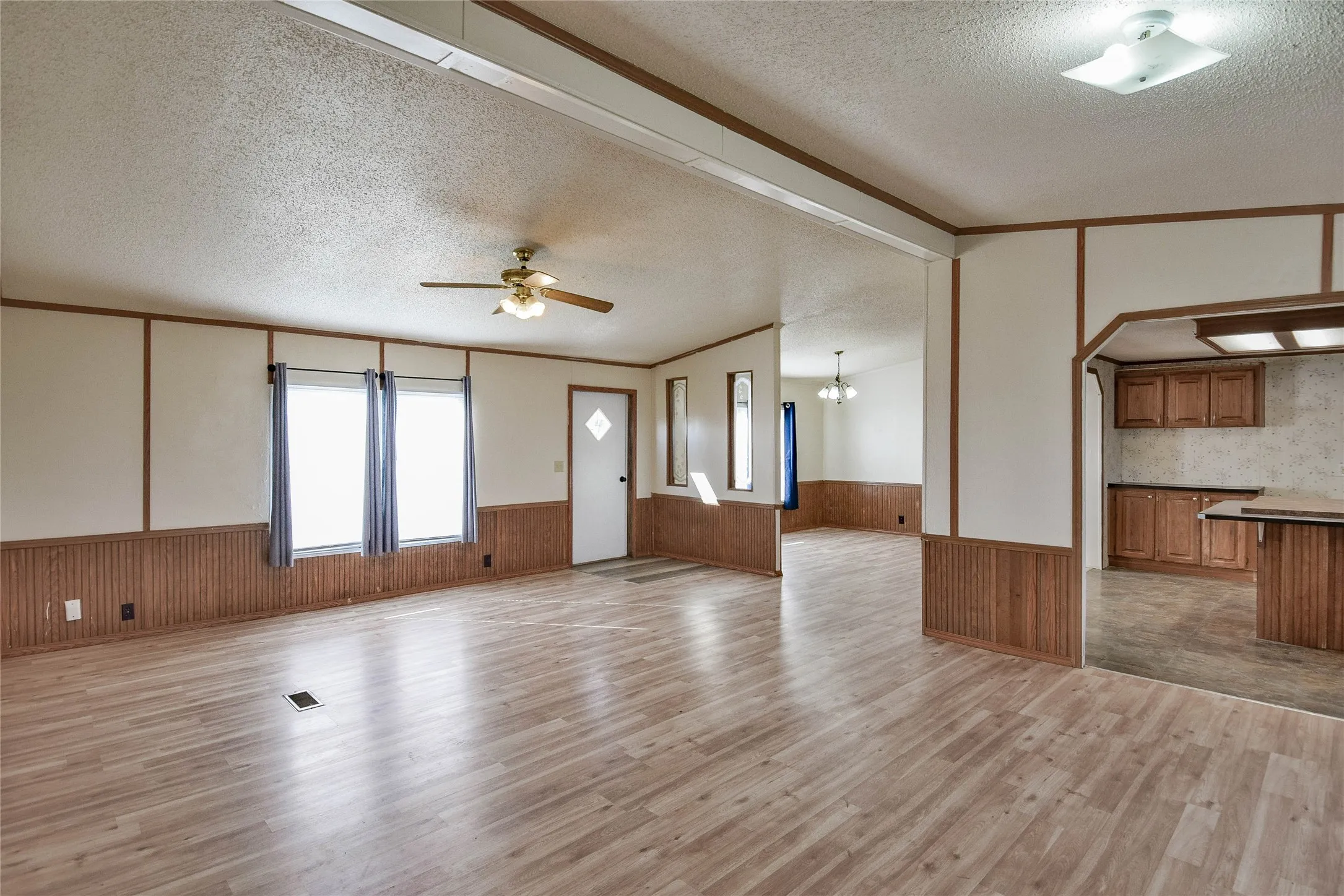 Spacious room with wood-finish flooring, two windows, a ceiling fan with integrated lighting, and a white entry door with a decorative diamond window