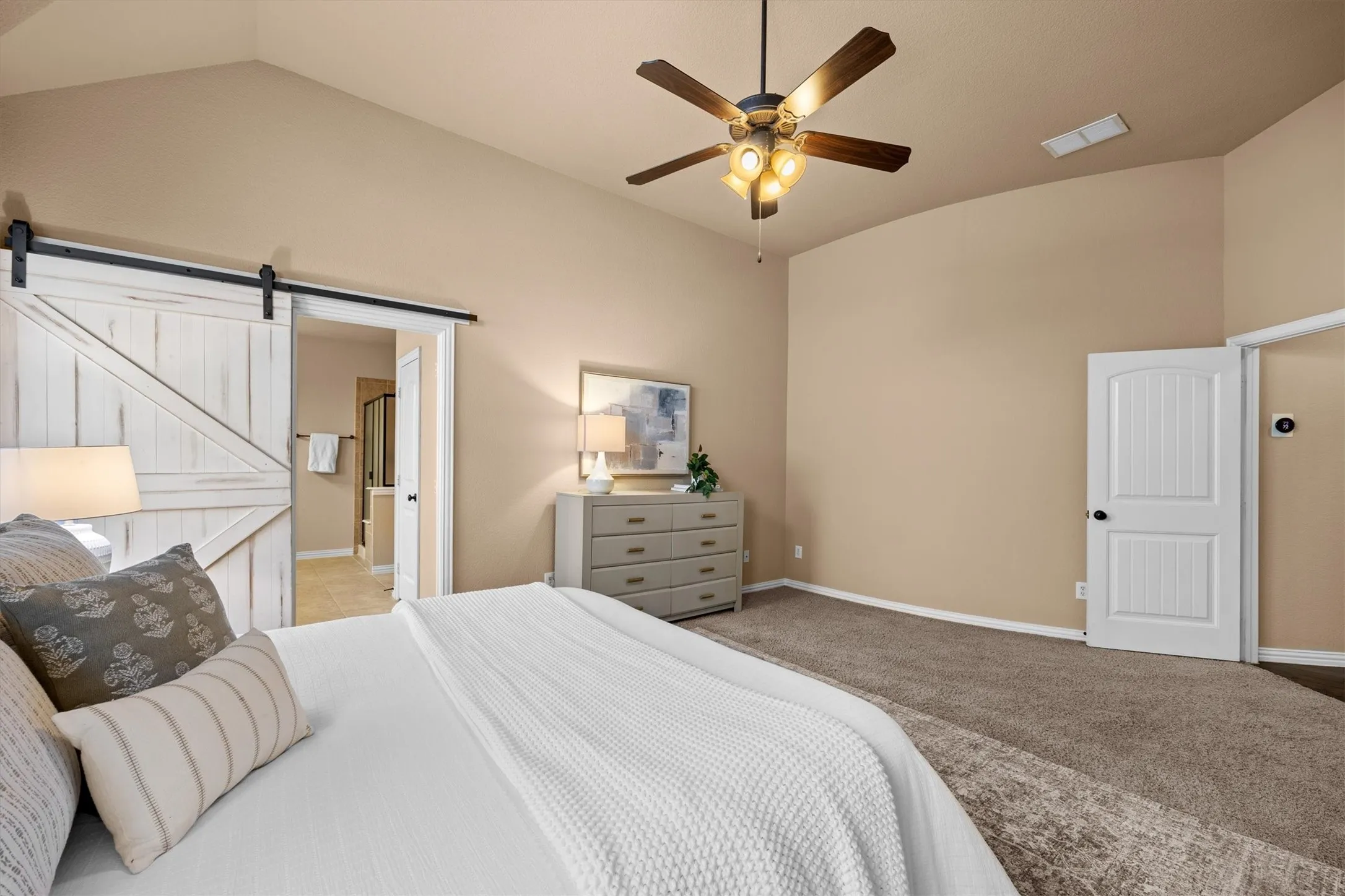 The spacious primary bedroom offers a relaxing retreat with a tray ceiling and sliding barn door to the bathroom.