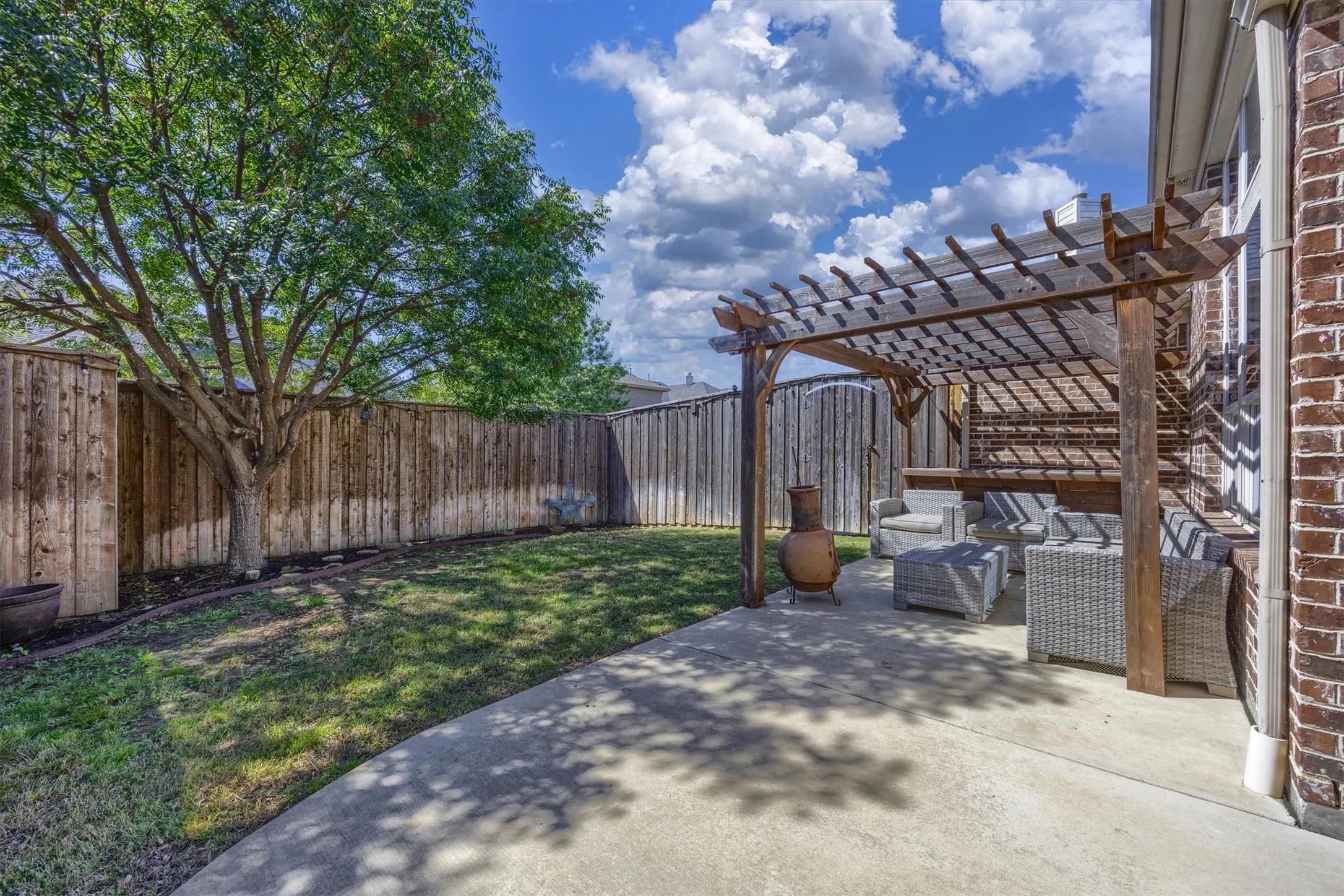 The pergola creates an inviting spot to relax beside the grassy backyard.