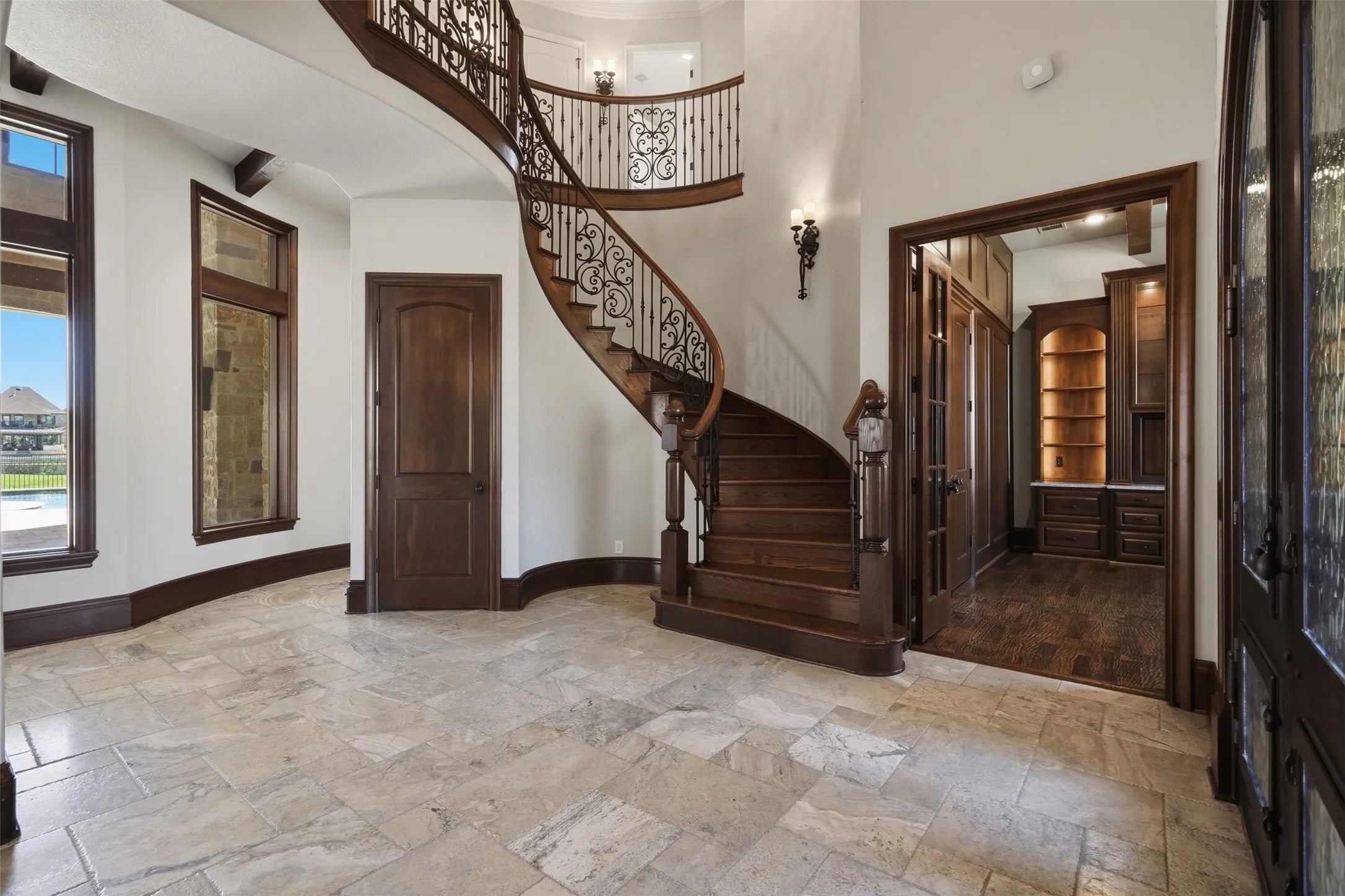 The entry makes an immediate impression with travertine floors laid in a Versailles pattern, a striking spiral staircase with wooden risers, and a ceiling accented with cedar beams.