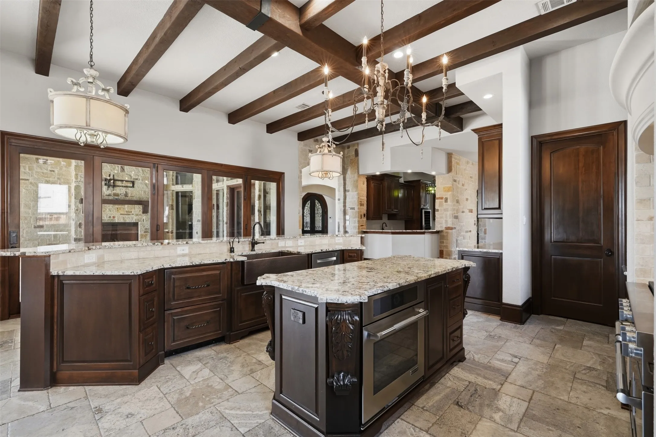 The travertine floors and cedar beamed ceiling carry seamlessly throughout the home, adding warmth and continuity to every space. In the kitchen, a copper farmhouse sink and a dedicated appliance garage beneath the microwave round out a thoroughly well-considered design.