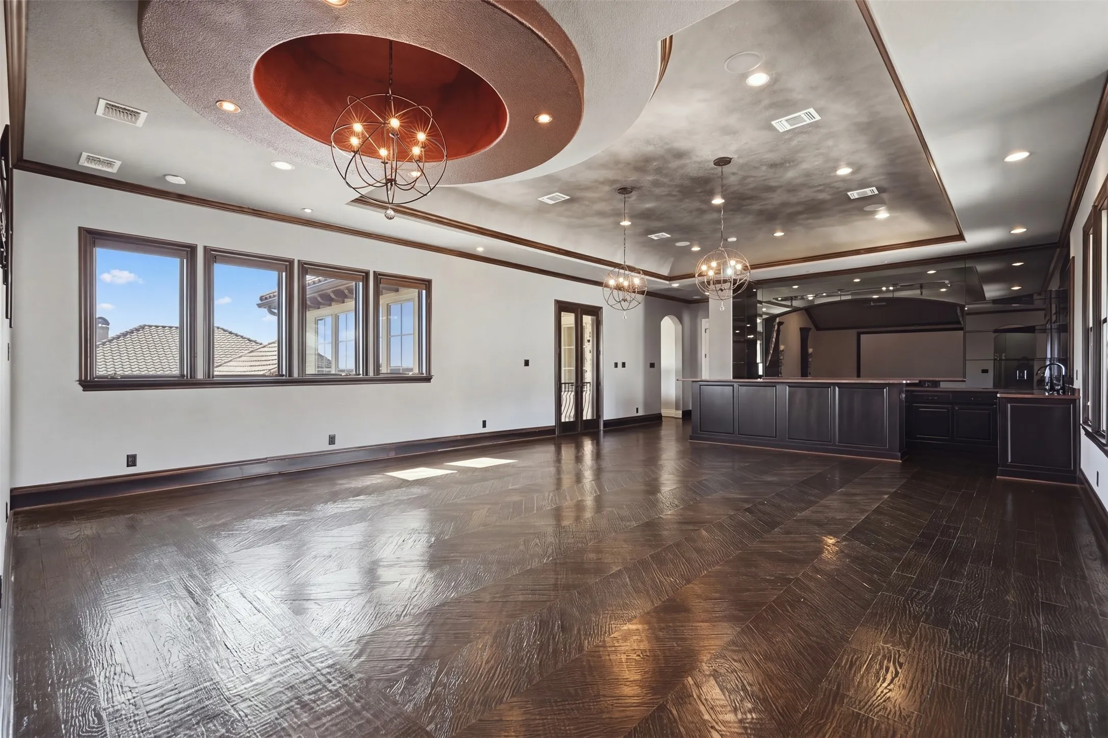 The upstairs game and media room are an entertainer's showpiece, finished with the polish of an upscale sports bar. Hand-scraped wood floors in a distinctive chevron pattern set the tone, while the full bar is appointed with granite countertops, a smoked glass backsplash, generous shelving, and a complete suite of appliances including a microwave, refrigerator, dishwasher, wine refrigerator, and a Sonic-style ice maker. The ceiling is equally impressive, featuring custom faux finishing, rope lighting, and three statement chandeliers.