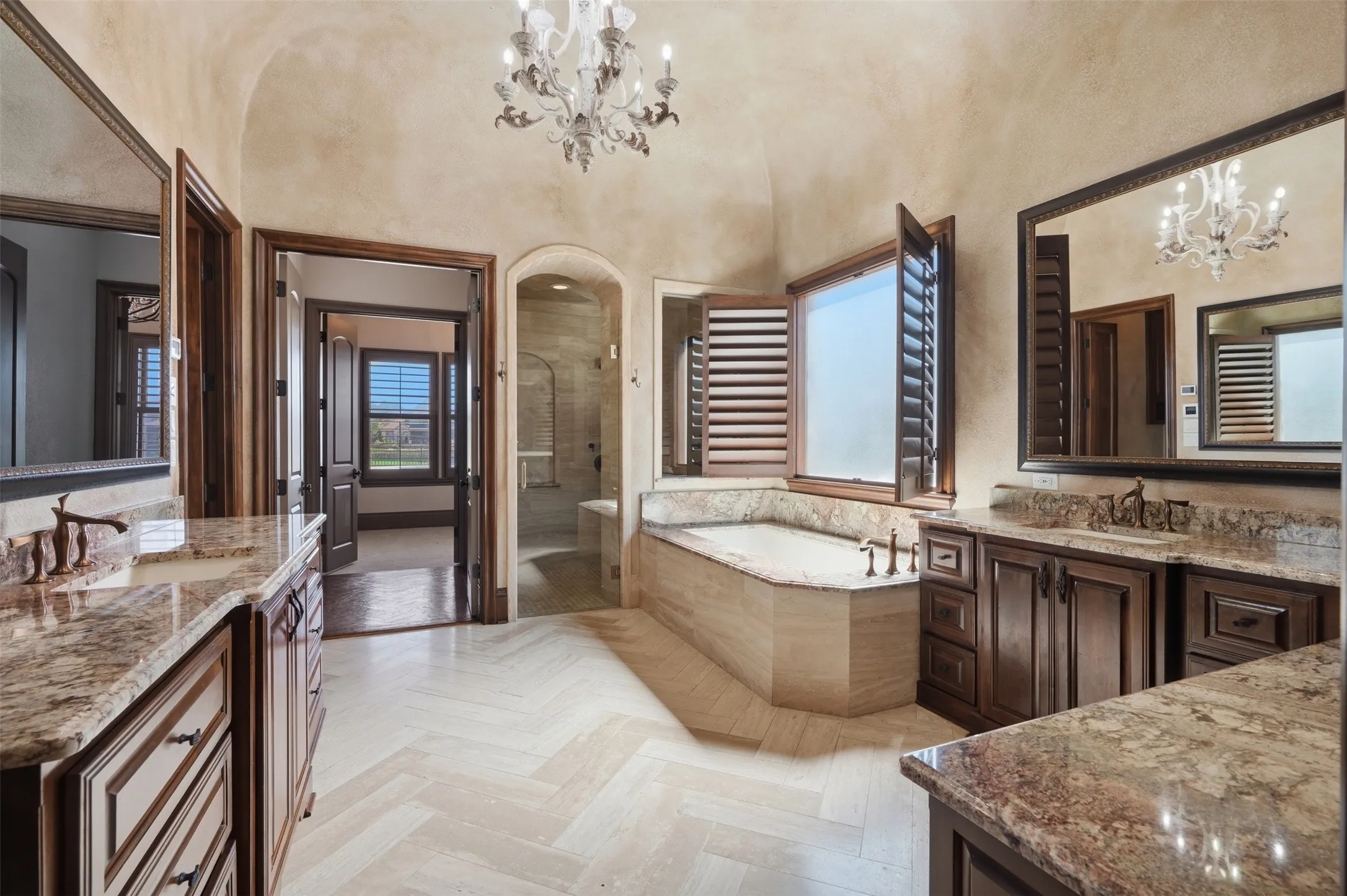 The primary bathroom features travertine floors in a herringbone pattern, a walk-in shower with three shower heads and a hand sprayer, dual vanities, a Toto toilet, and a custom ceiling treatment with chandelier.
