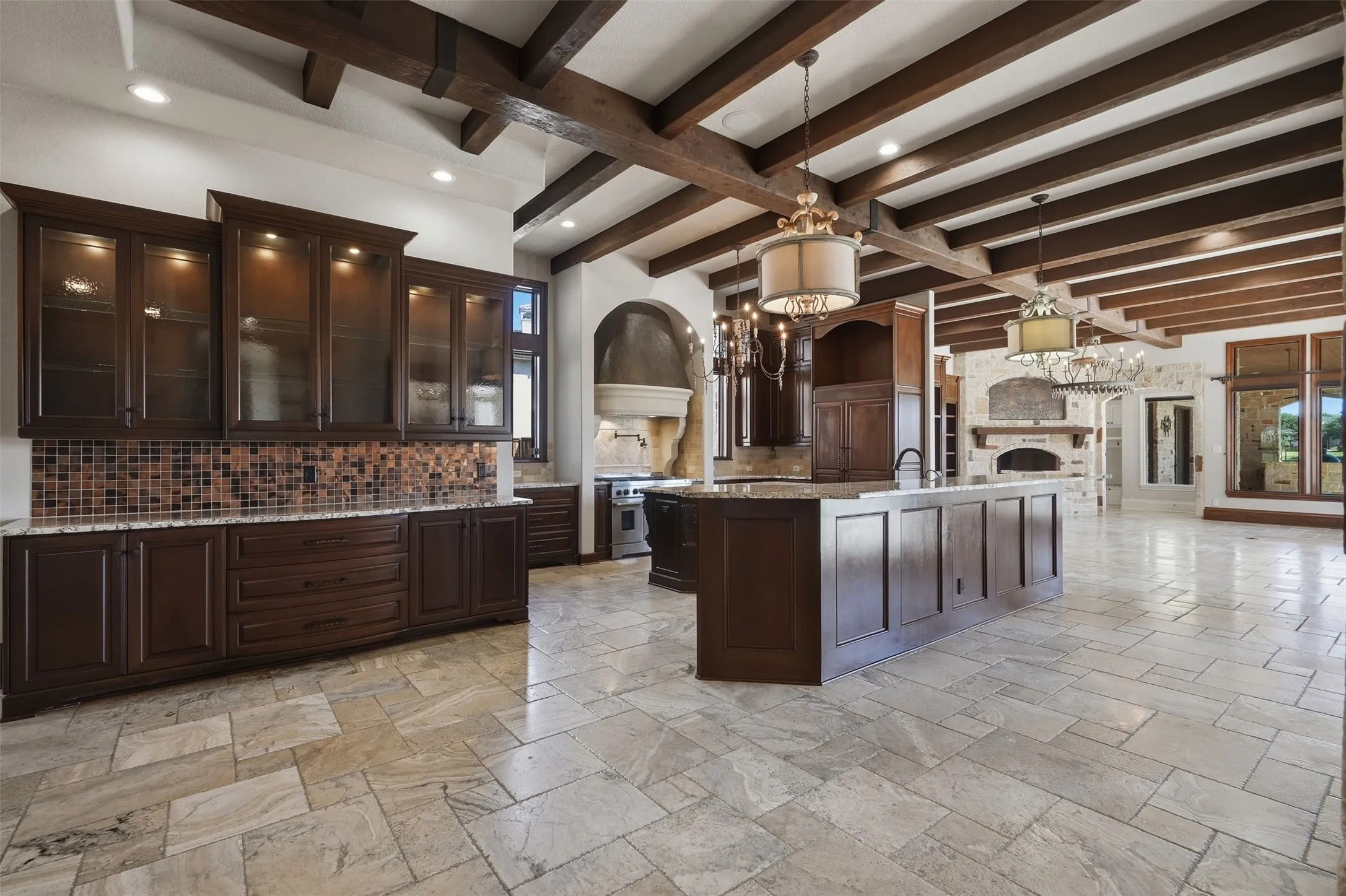 The kitchen is equipped with a large walk-in pantry, pot filler, and a full suite of Jenn-Air stainless appliances including three ovens, a large cooktop with grill, and a warming drawer. The built-in Jenn-Air refrigerator is seamlessly integrated behind custom cabinetry doors for a clean, cohesive look. The design carries intentionally from the kitchen into the family room, with matching light fixtures and custom copper details — a copper hood vent over the cooktop and a matching copper inset on the family room fireplace — creating a cohesive and refined flow between the two spaces.