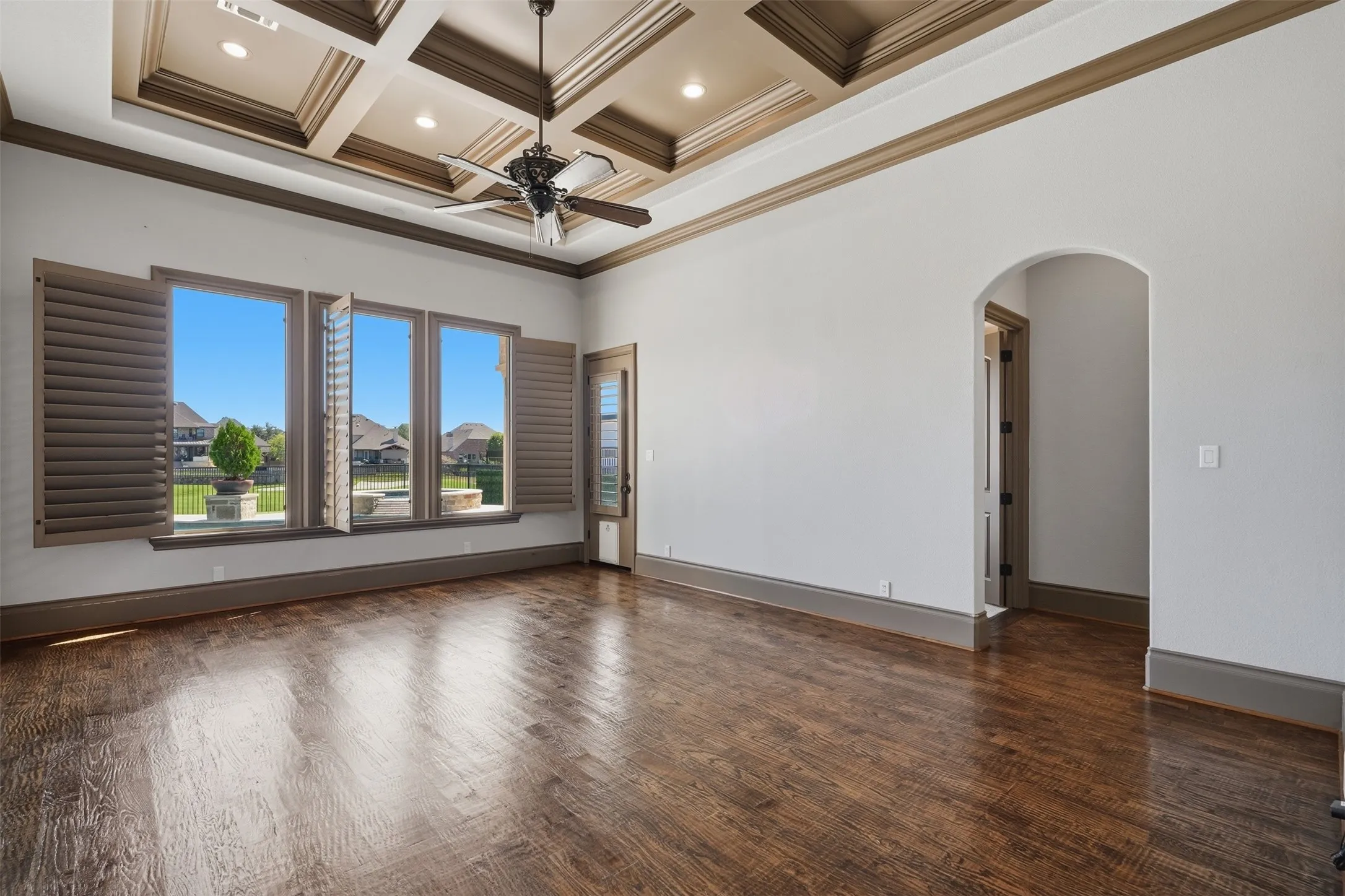 The primary suite features hand-scraped wood floors, a coffered ceiling with wood beams, and a wall of windows overlooking the golf course. A private exterior door leads directly to the covered patio.