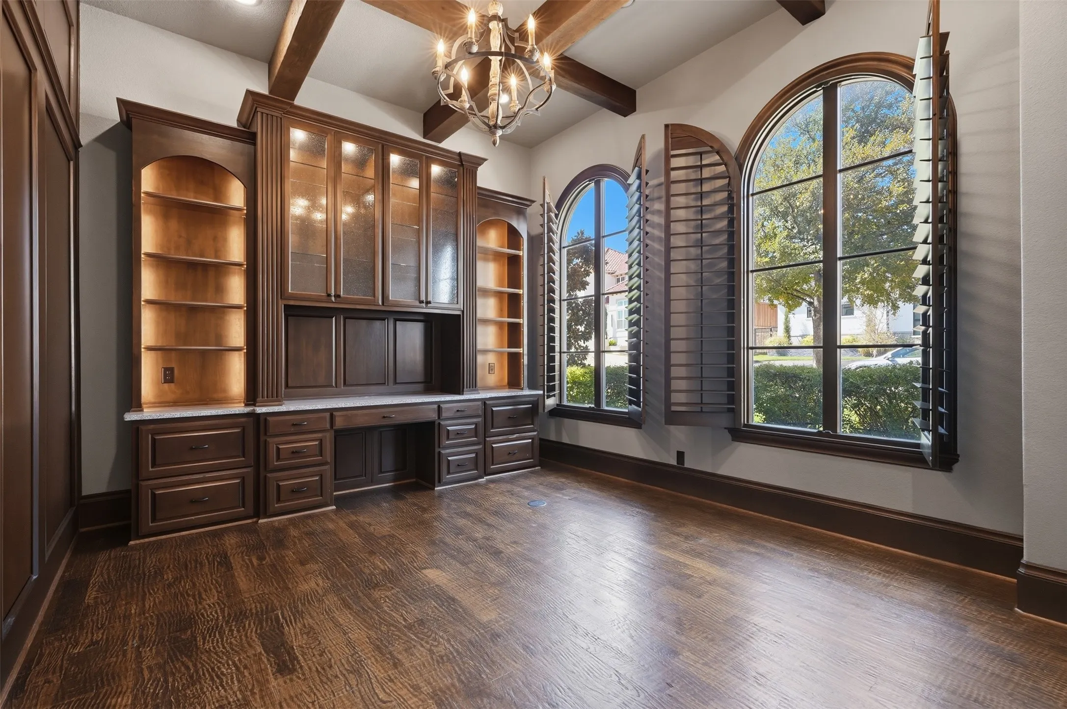 The study features hand-scraped hardwood floors, a cedar beamed ceiling, and custom built-in cabinetry with glass doors and lighted shelving — plus a hidden passage door connecting to the utility room, a detail as functional as it is memorable.