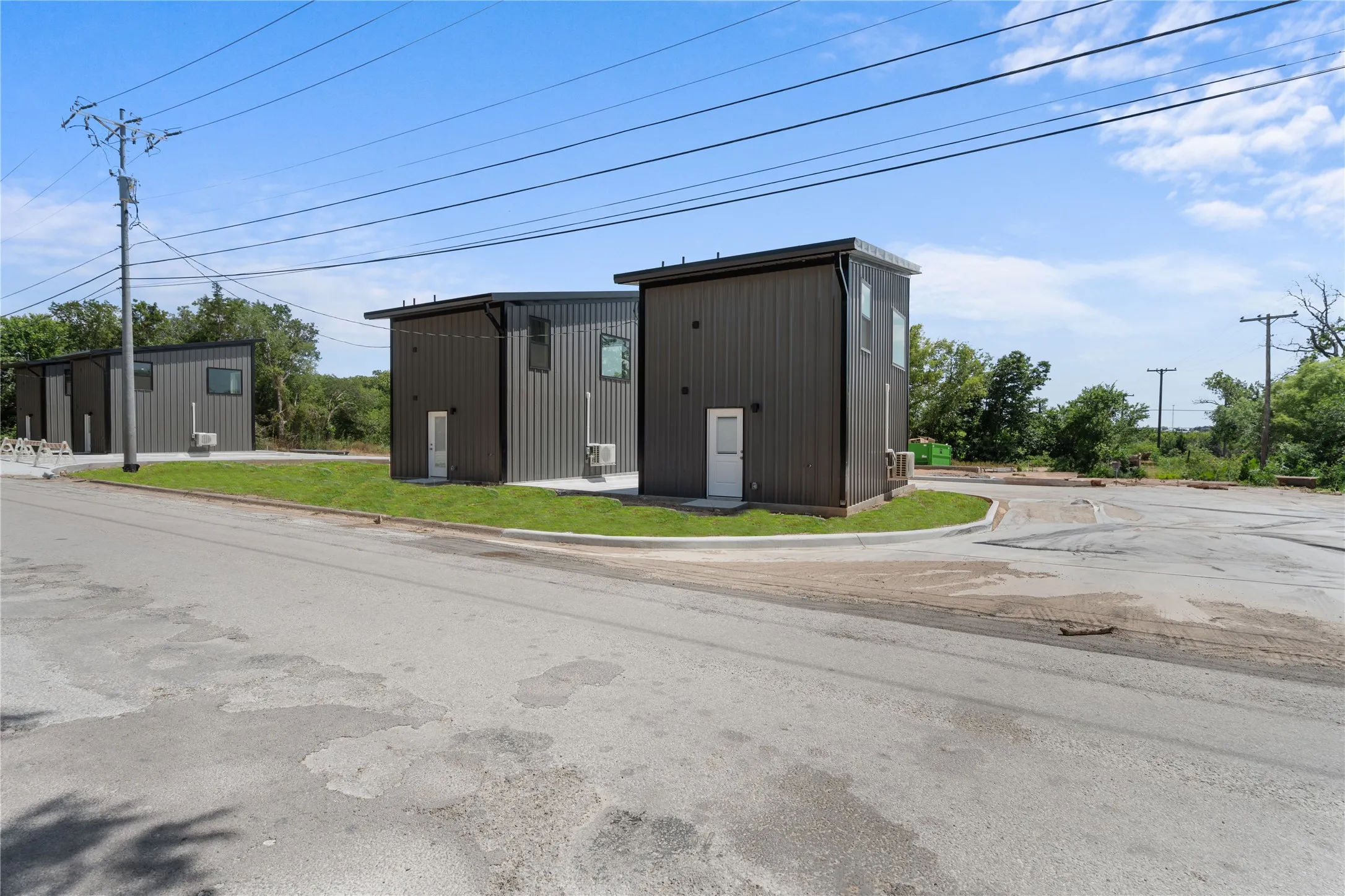 Modern exterior featuring dark vertical siding, white entry doors, compact patios, and an asphalt parking area