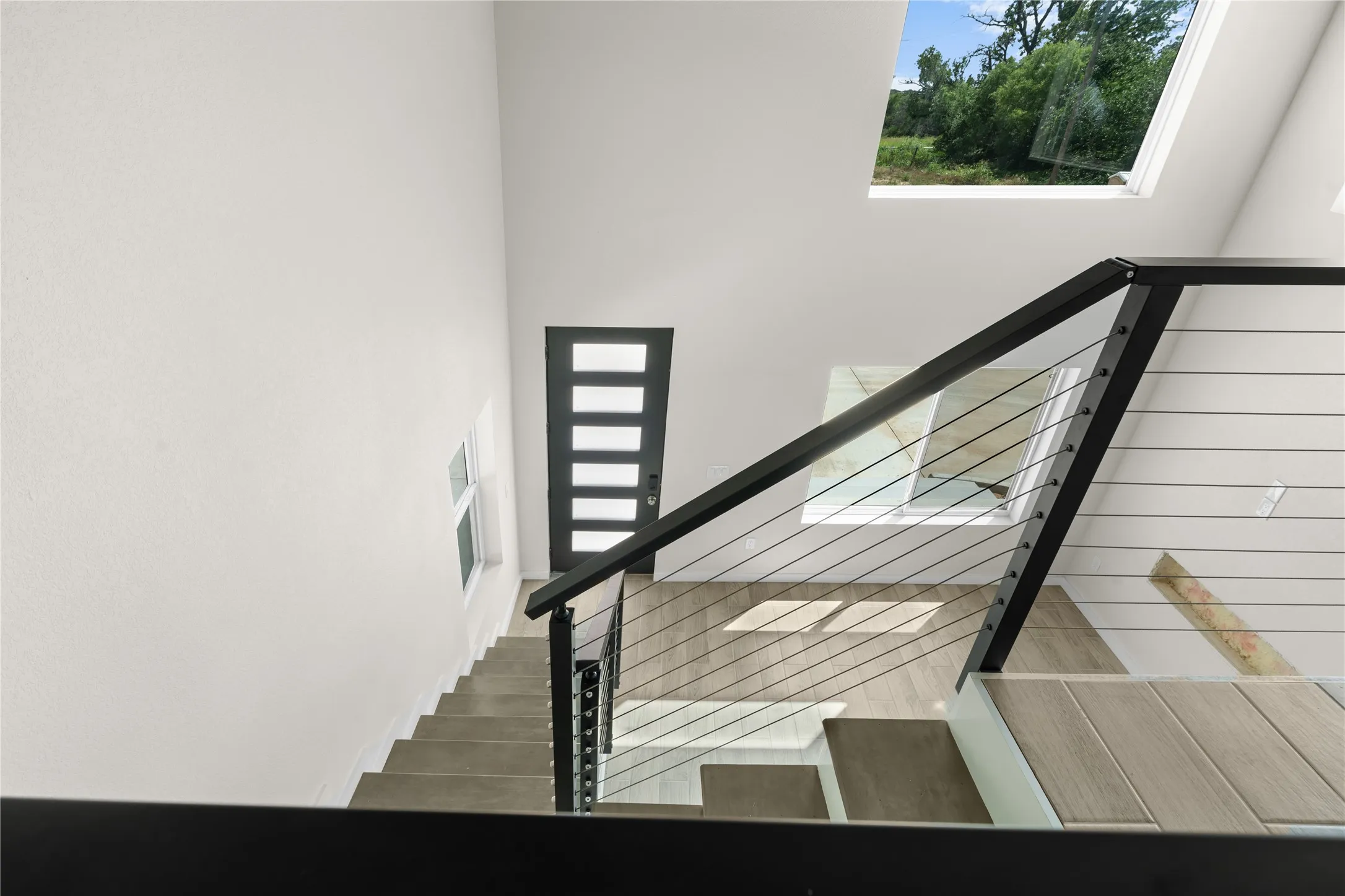 Stairwell featuring a contemporary railing with metal cables, wood-finish flooring, and white walls