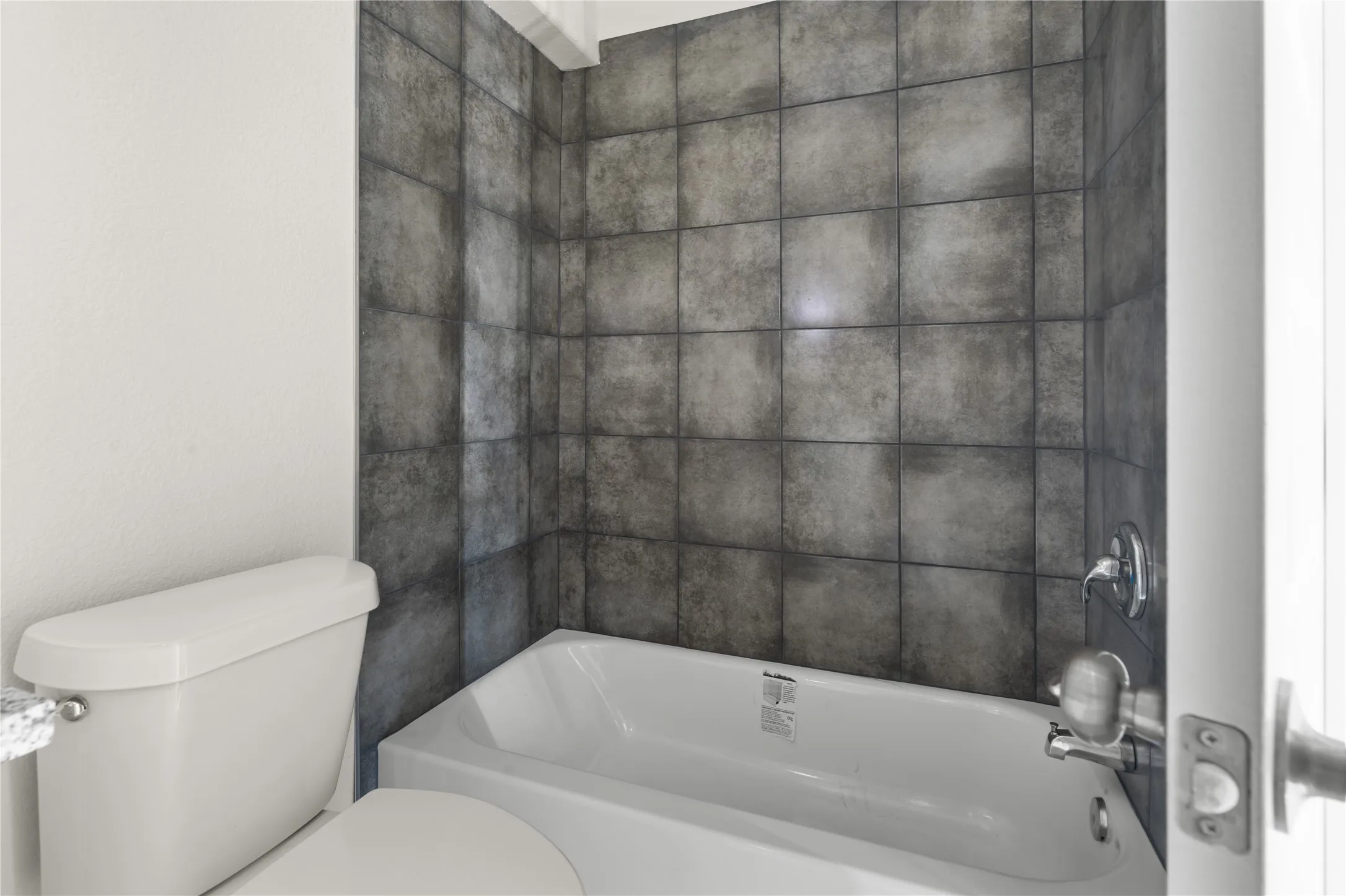 White drop-in bathtub with chrome fixtures and dark-toned wall tiles