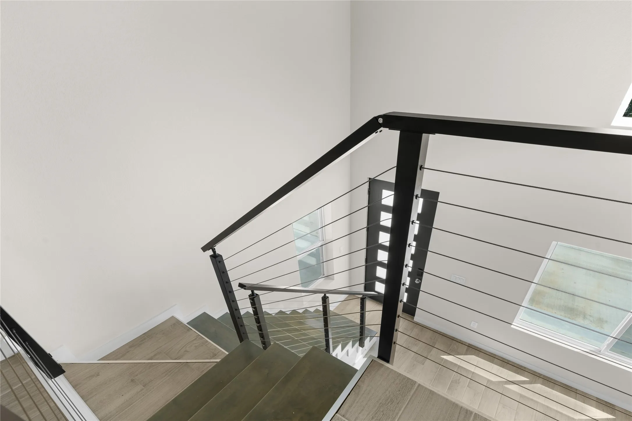 Modern cable railing system with black handrails, light wood-finish flooring, and a contemporary entry door with frosted glass inserts
