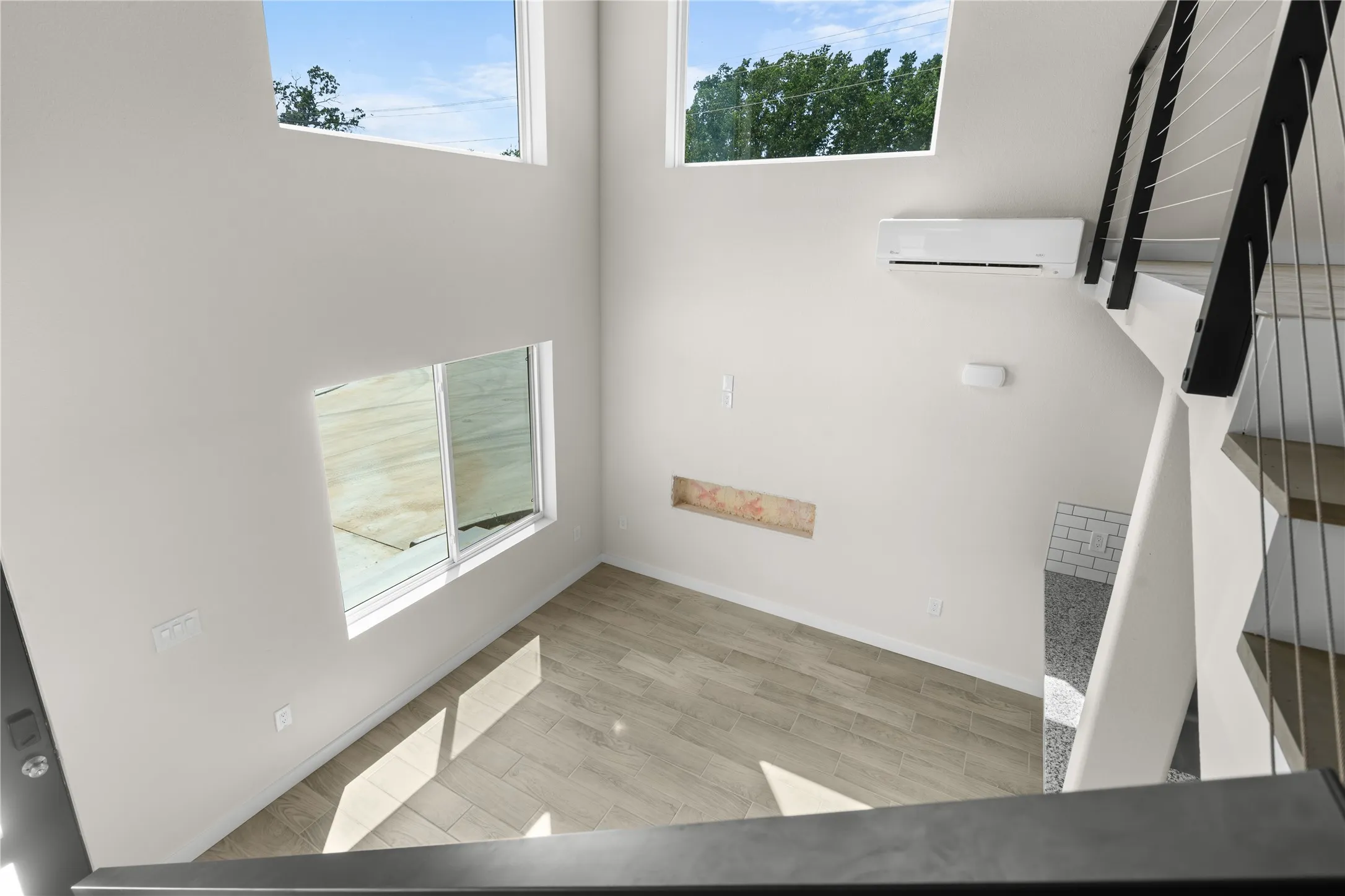 Two-story ceiling, large windows, wood-finish flooring, built-in shelf, and contemporary staircase with cable railing