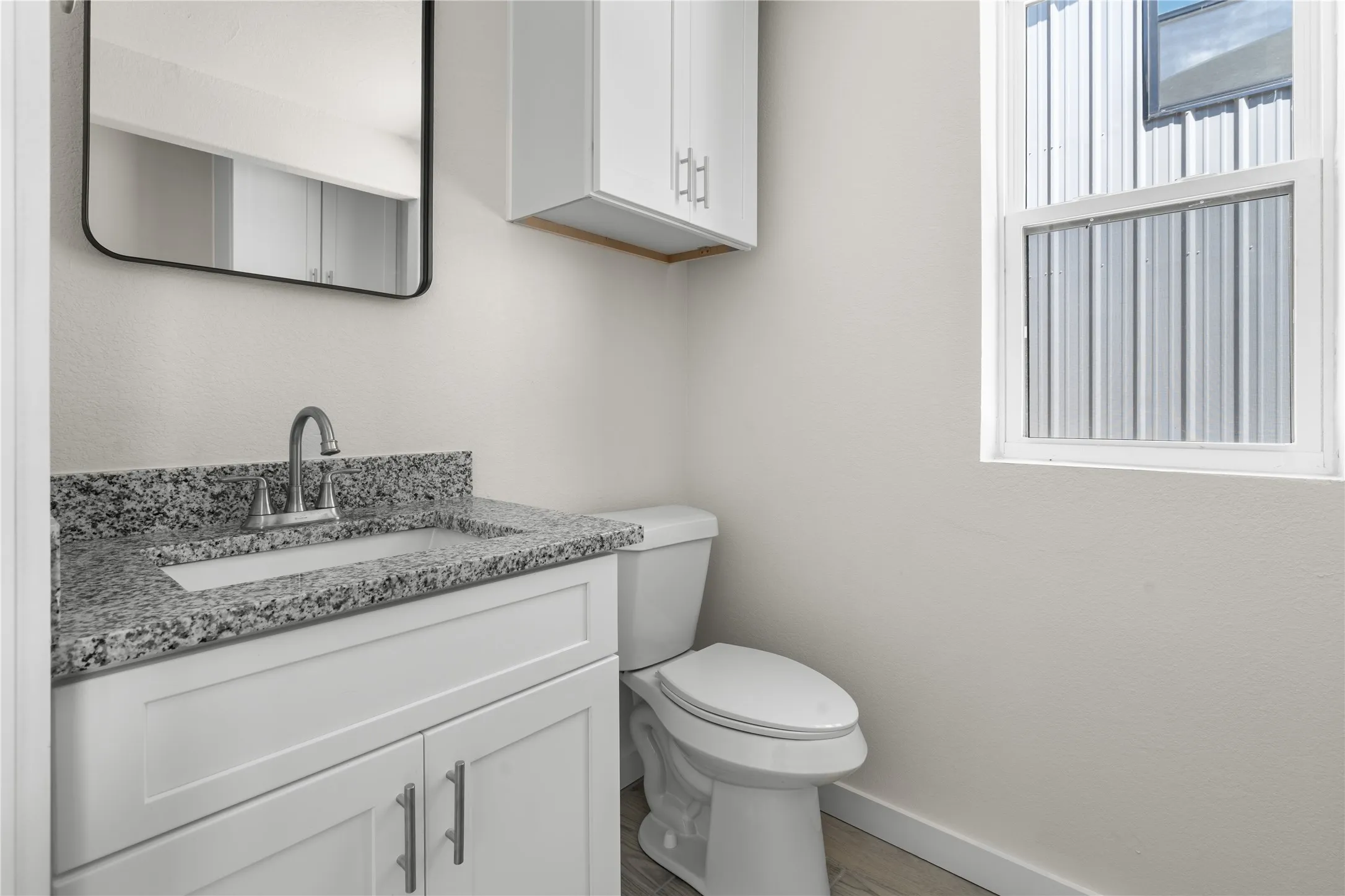 White vanity with shaker-style cabinetry, granite countertop, undermount sink, and wall-mounted mirror