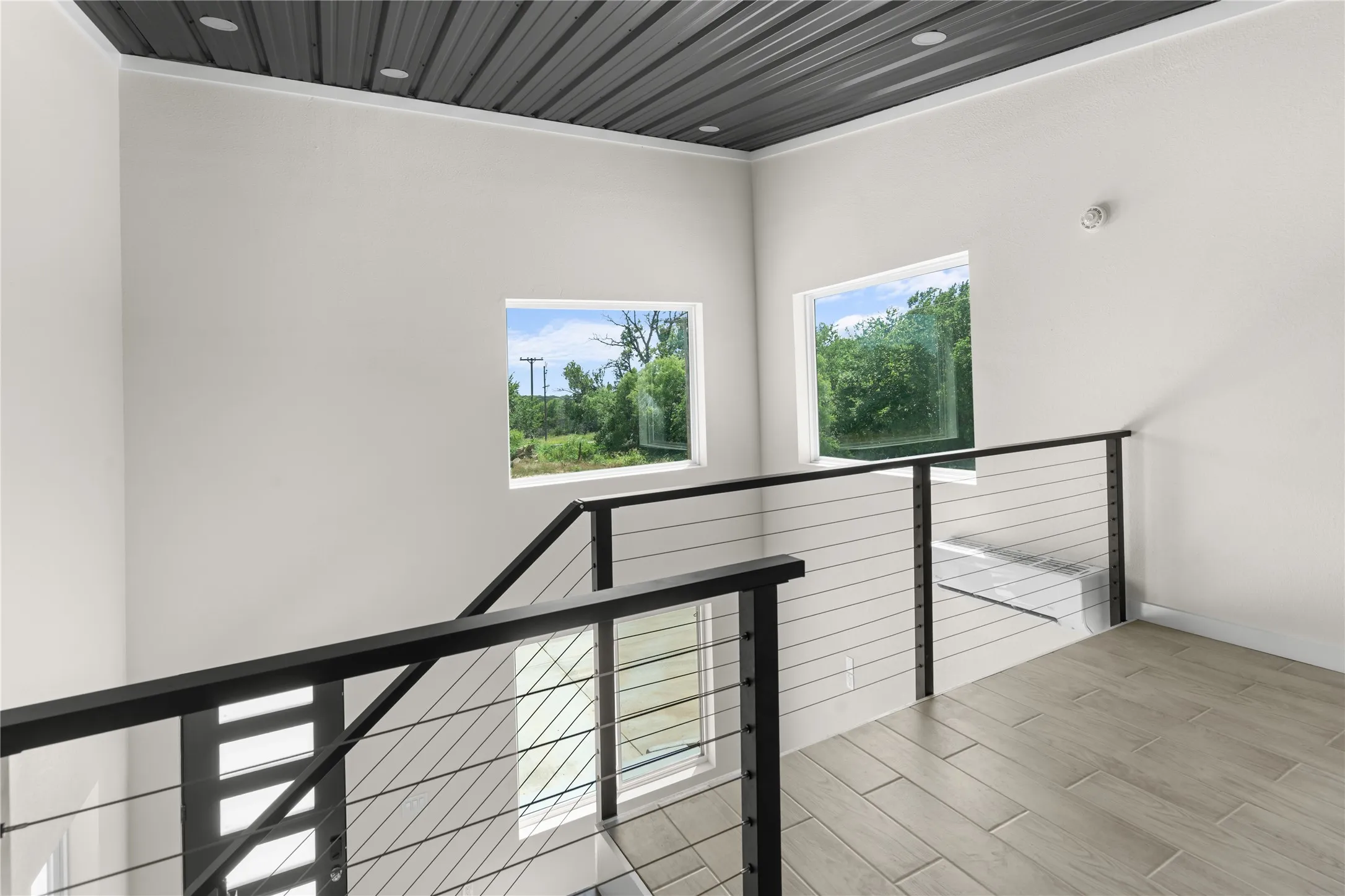 Modern cable railing system, wood-finish flooring, recessed lighting, and a corrugated metal ceiling
