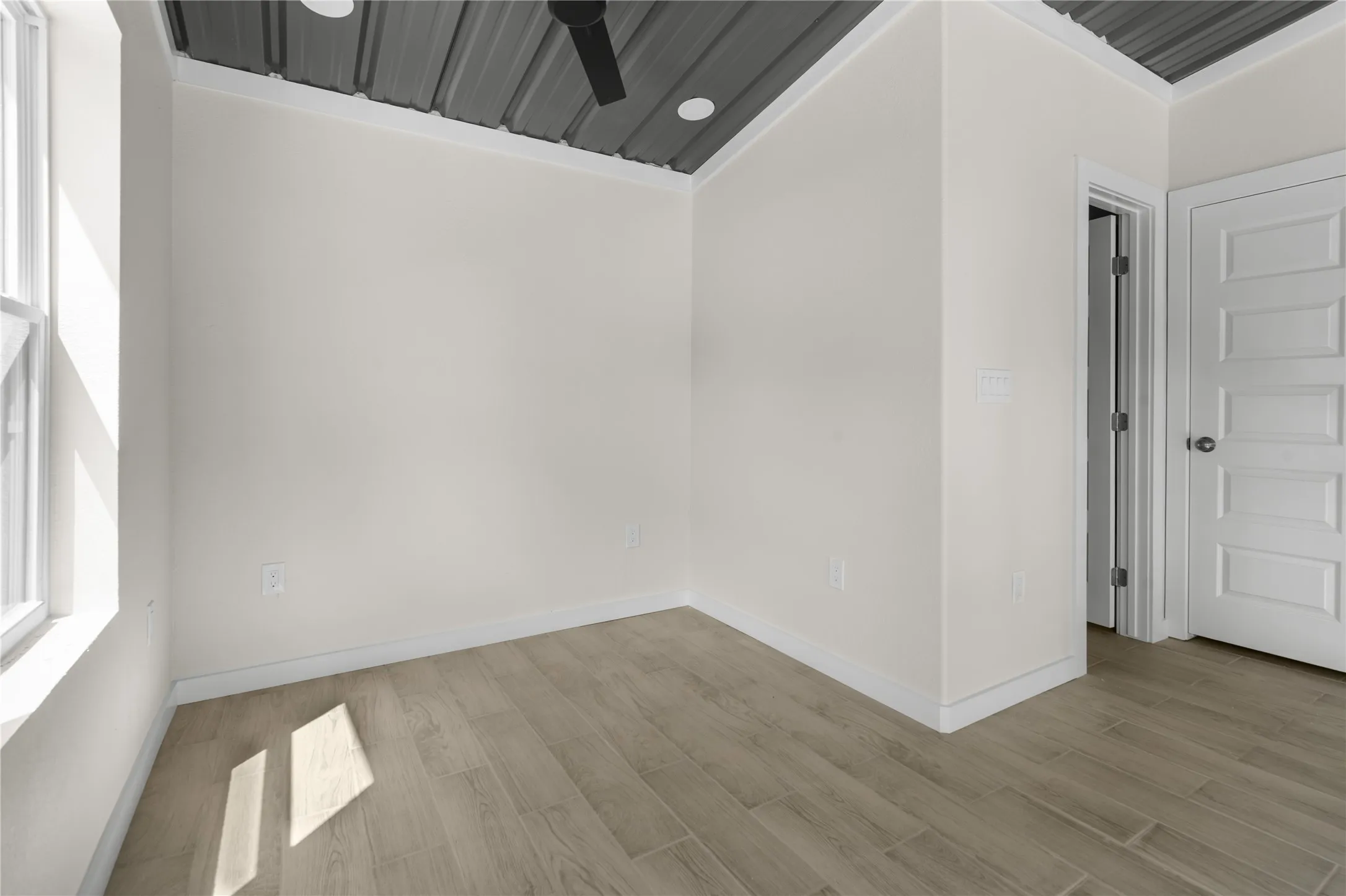 Wood-finish flooring, white paneled interior door, corrugated metal ceiling with recessed lighting, and a ceiling fan