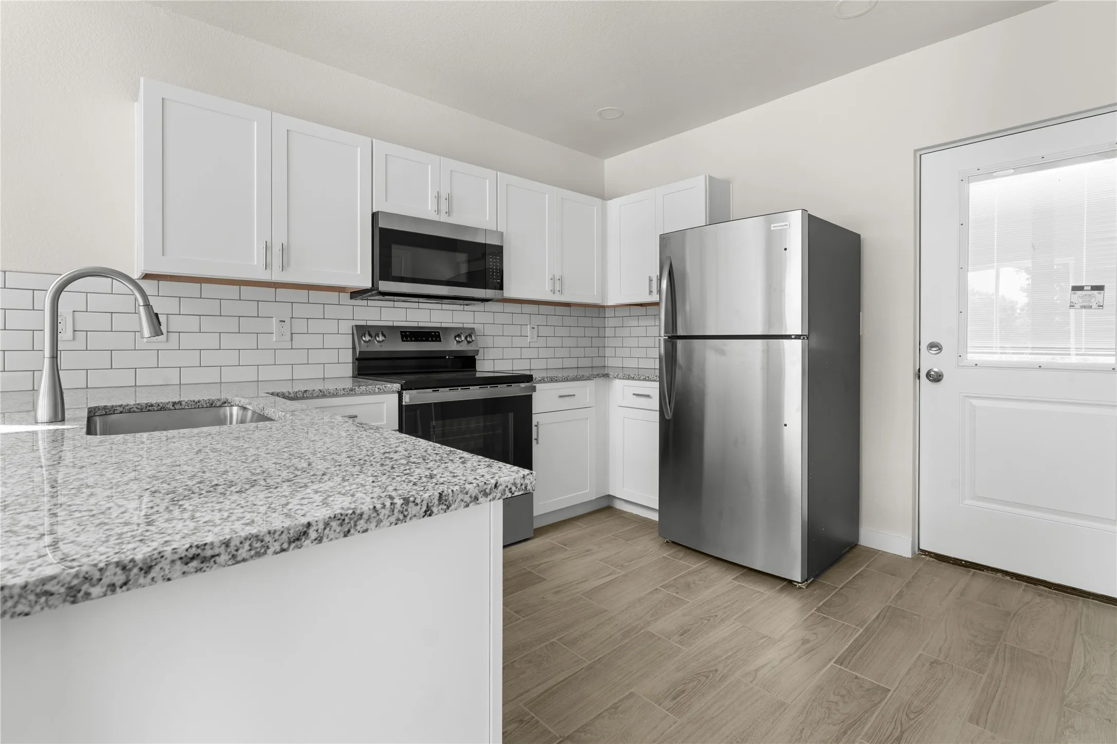 Kitchen featuring white cabinetry, stainless steel appliances, granite countertops, a subway tile backsplash, and wood-finish flooring