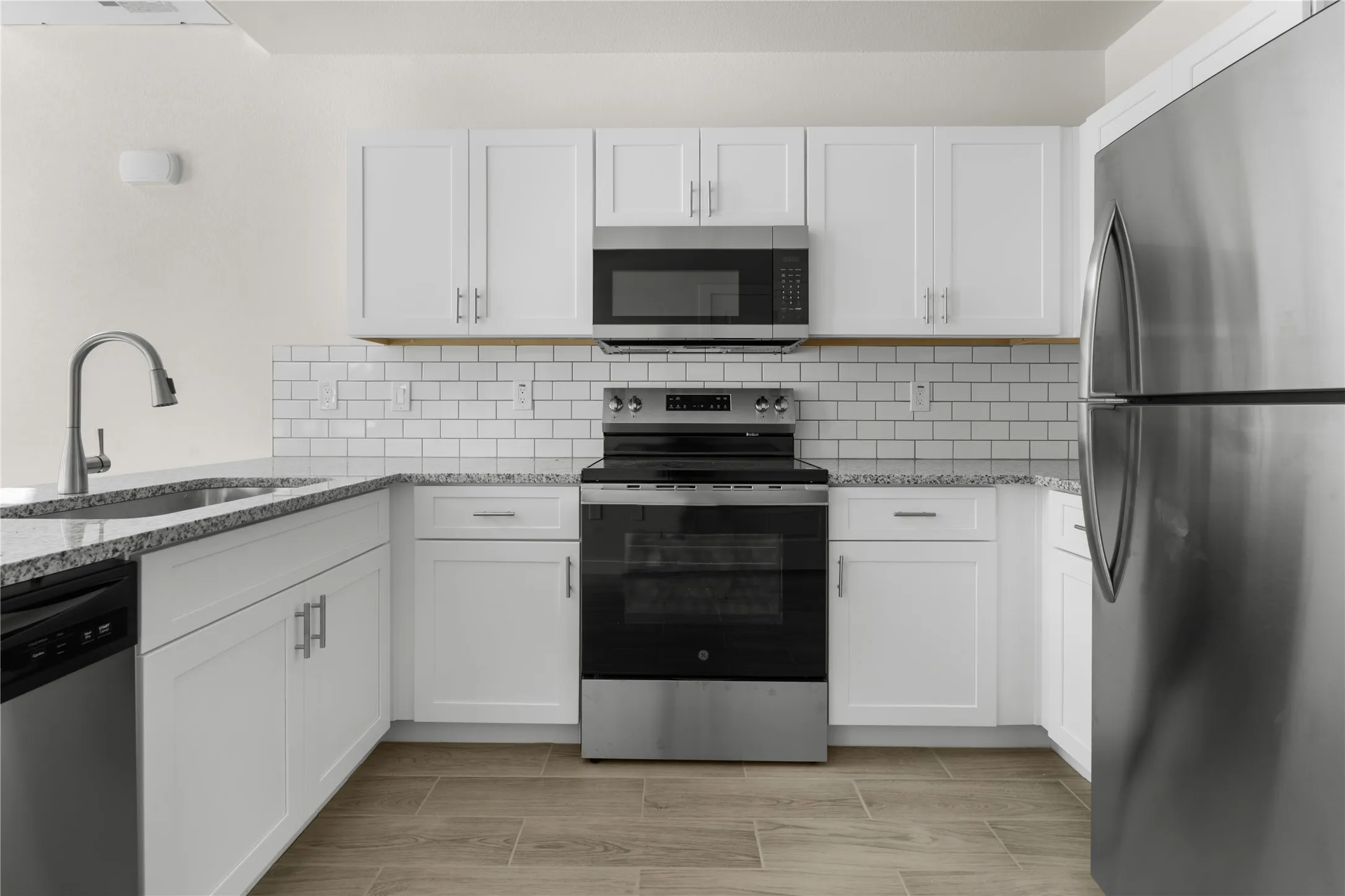 Kitchen featuring white cabinetry, light-toned countertops, a subway tile backsplash, stainless steel appliances, and wood-finish flooring