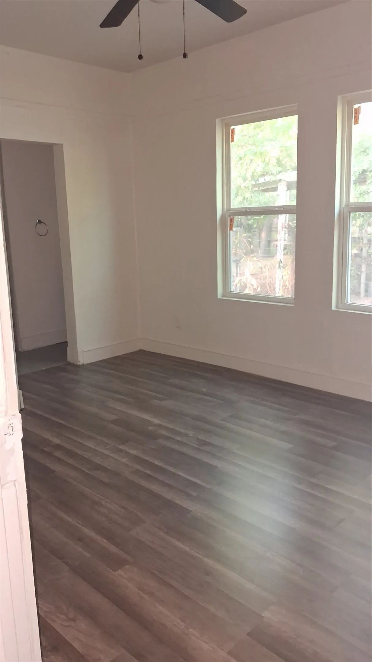 Wood-finish flooring, white walls, two windows, and a ceiling fan