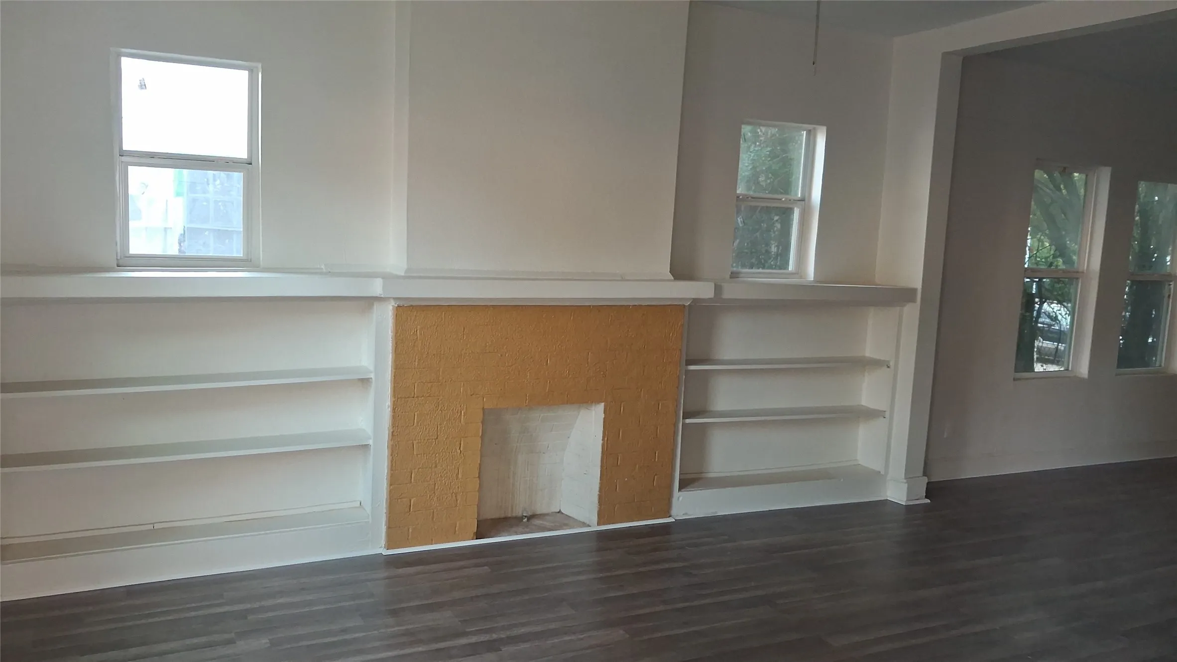 Built-in shelving flanking a textured fireplace surround, with multiple windows and wood-finish flooring