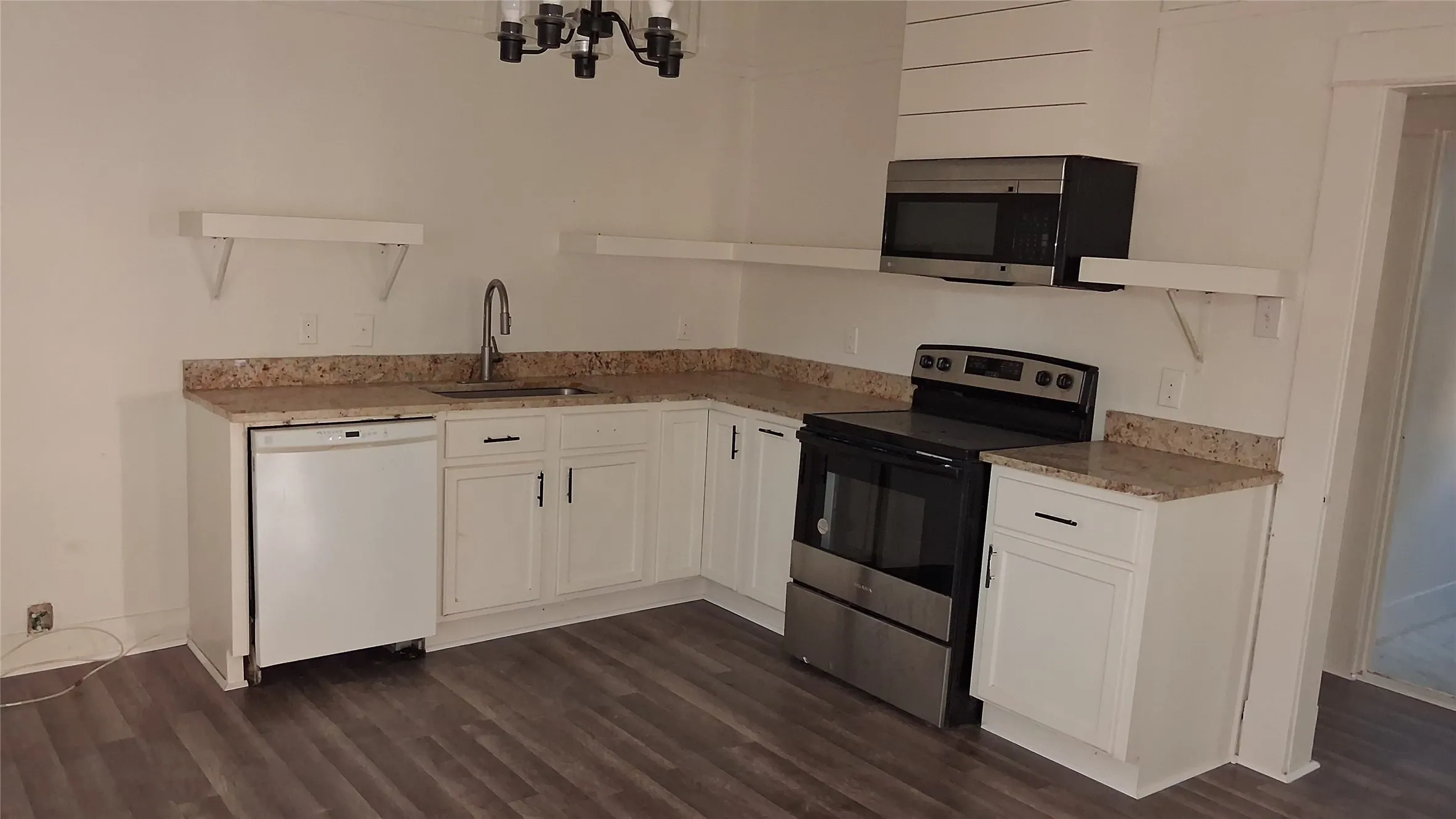 White cabinetry with black hardware, stone-finish countertops, stainless steel appliances, wood-finish flooring, and a decorative light fixture