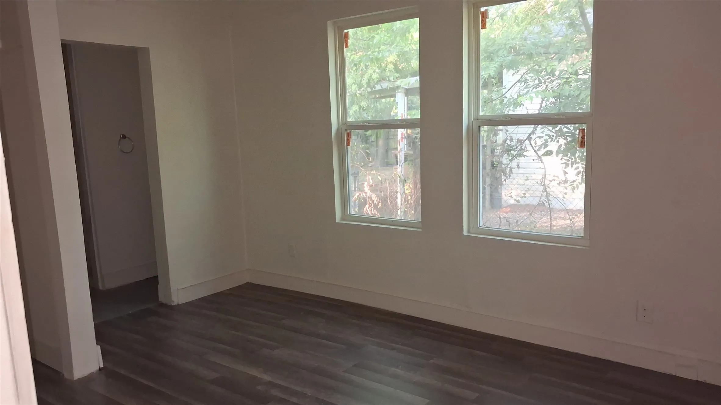 Wood-finish flooring with white baseboards, white walls, and two windows