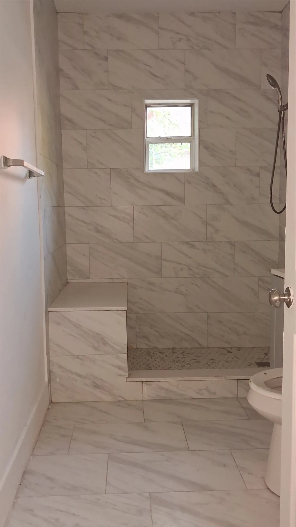 Tiled shower with a built-in bench, handheld shower fixture, and a window for natural light