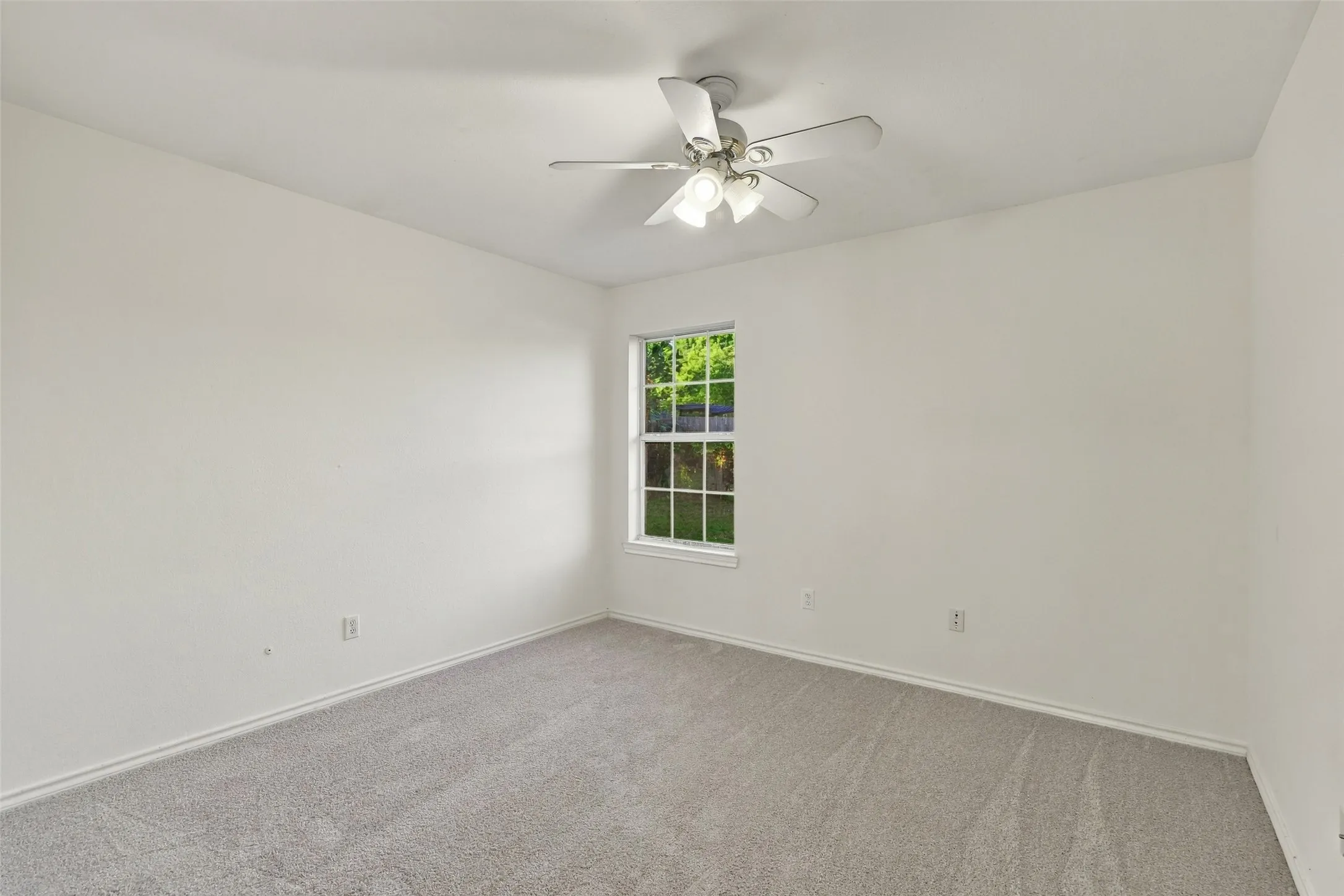 Bedroom: Versatile carpeted bedroom featuring neutral walls, a ceiling fan, and a window with views of the greenery outside.